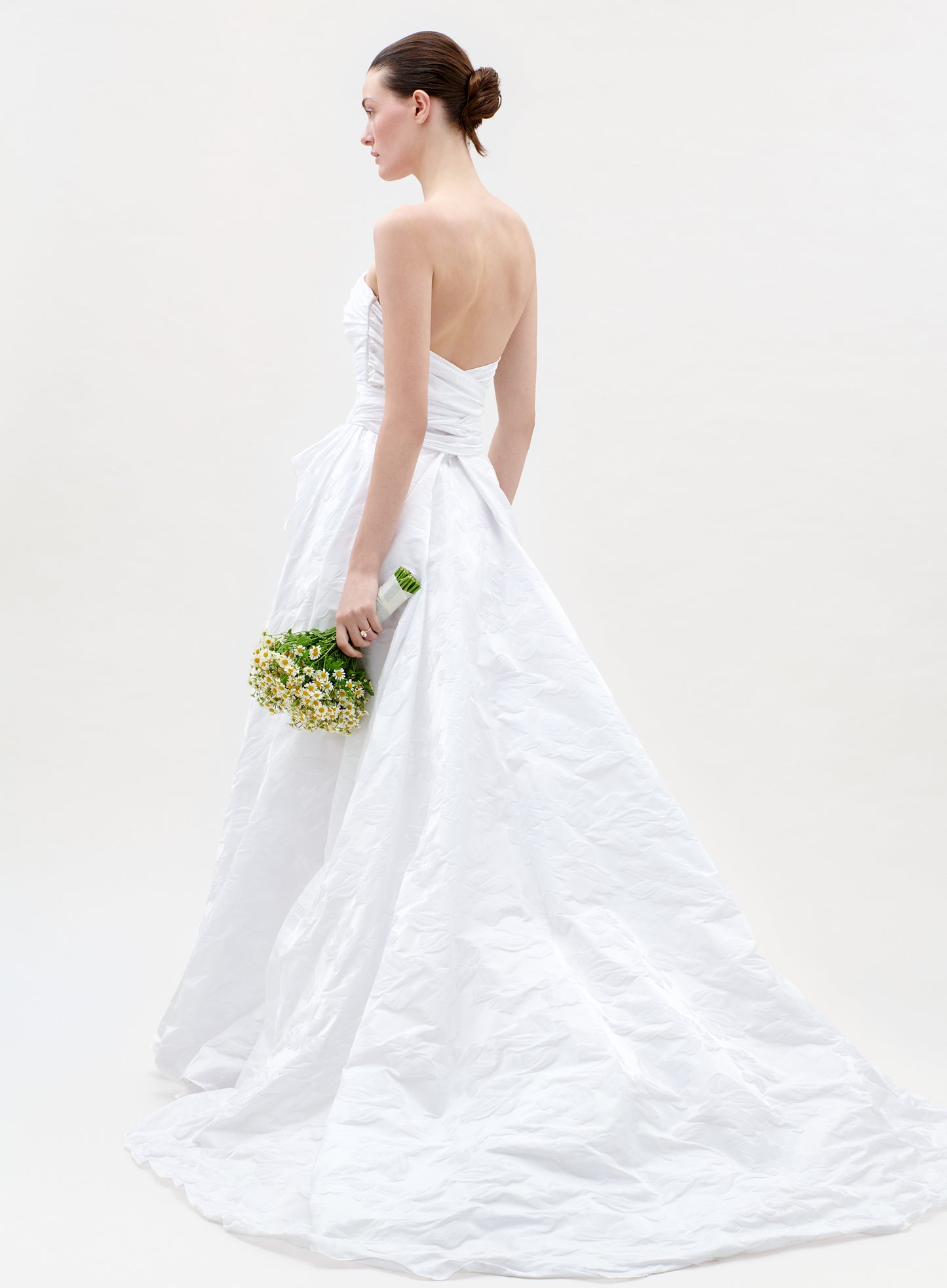 Woman in a white wedding dress holding a bouquet on a plain background