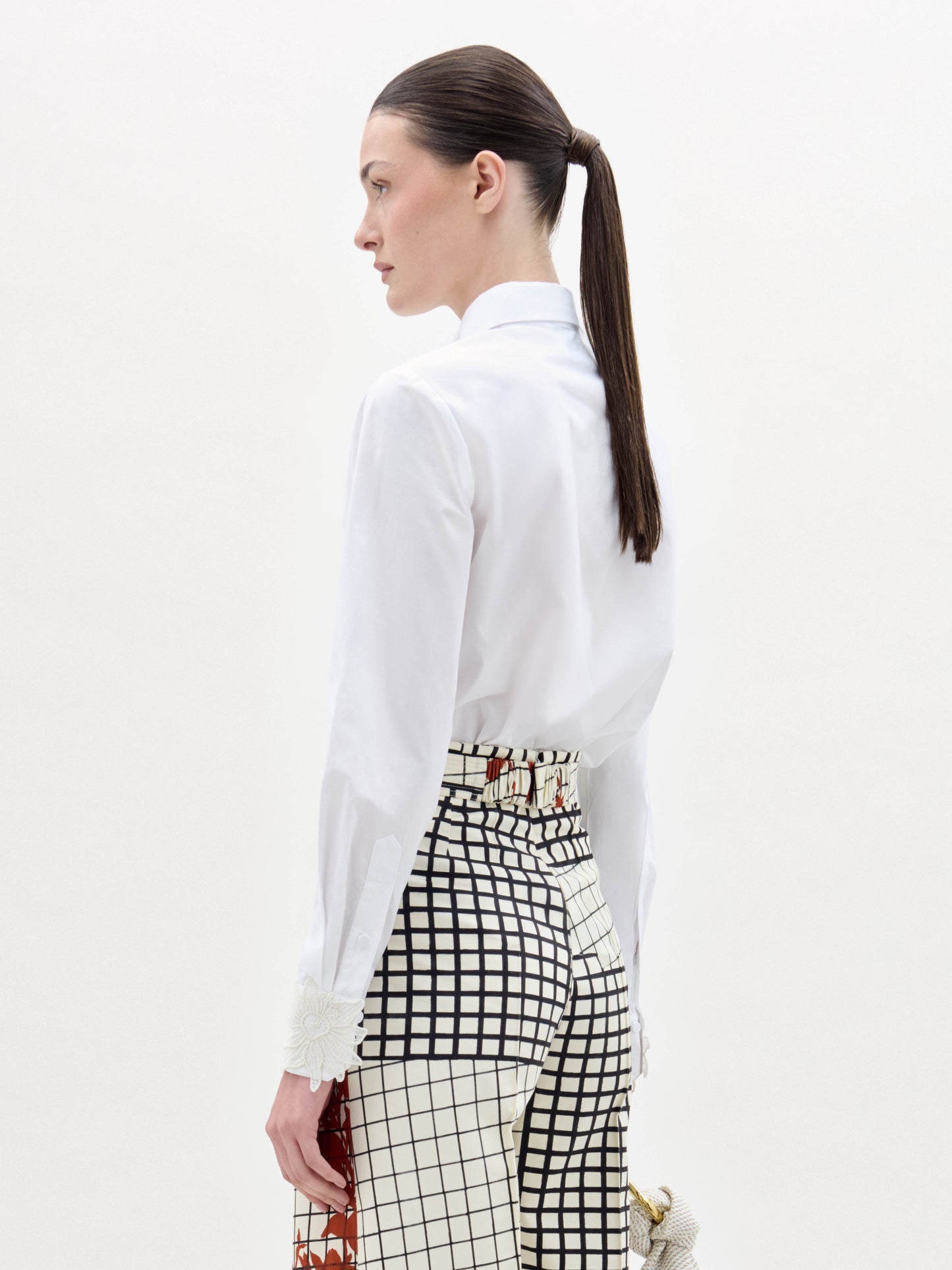 A woman stands against a white background wearing the Naroa Blouse, paired with high-waisted grid-and-floral print pants and a wide belt featuring a gold buckle.