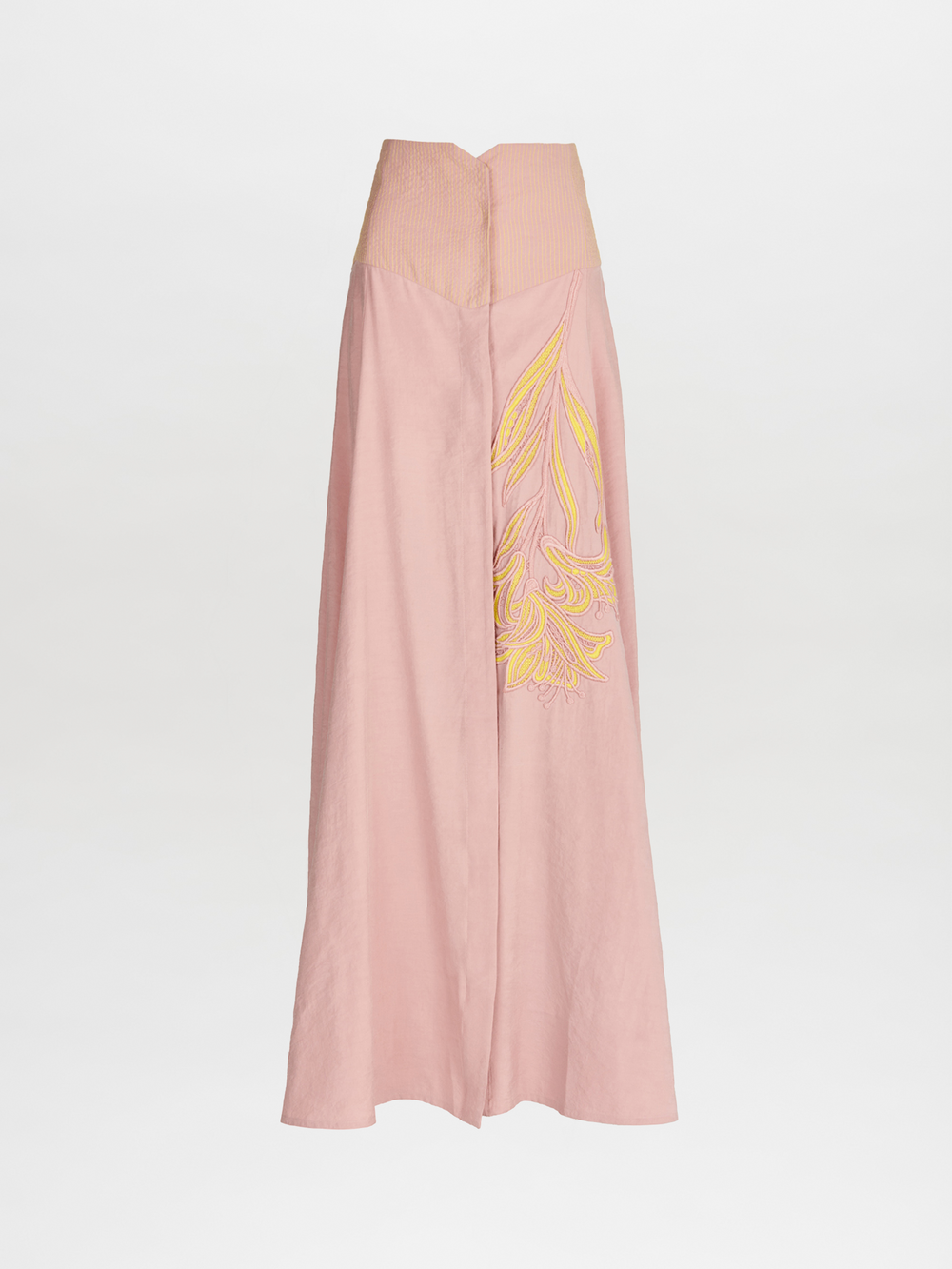 The Modena Skirt Pink by Silvia Tcherassi is a high-waisted, floor-length maxi skirt in light pink, featuring yellow floral applique on one side, a structured waistband, and a central seam. It's crafted from soft cupro against a plain white background.