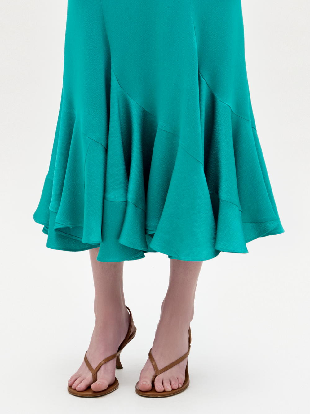 Only the lower legs and feet are visible as someone models the SVT DESIGNS Marlene Skirt, a teal ruffled A-line midi skirt, paired with brown strappy sandals against a plain light background.