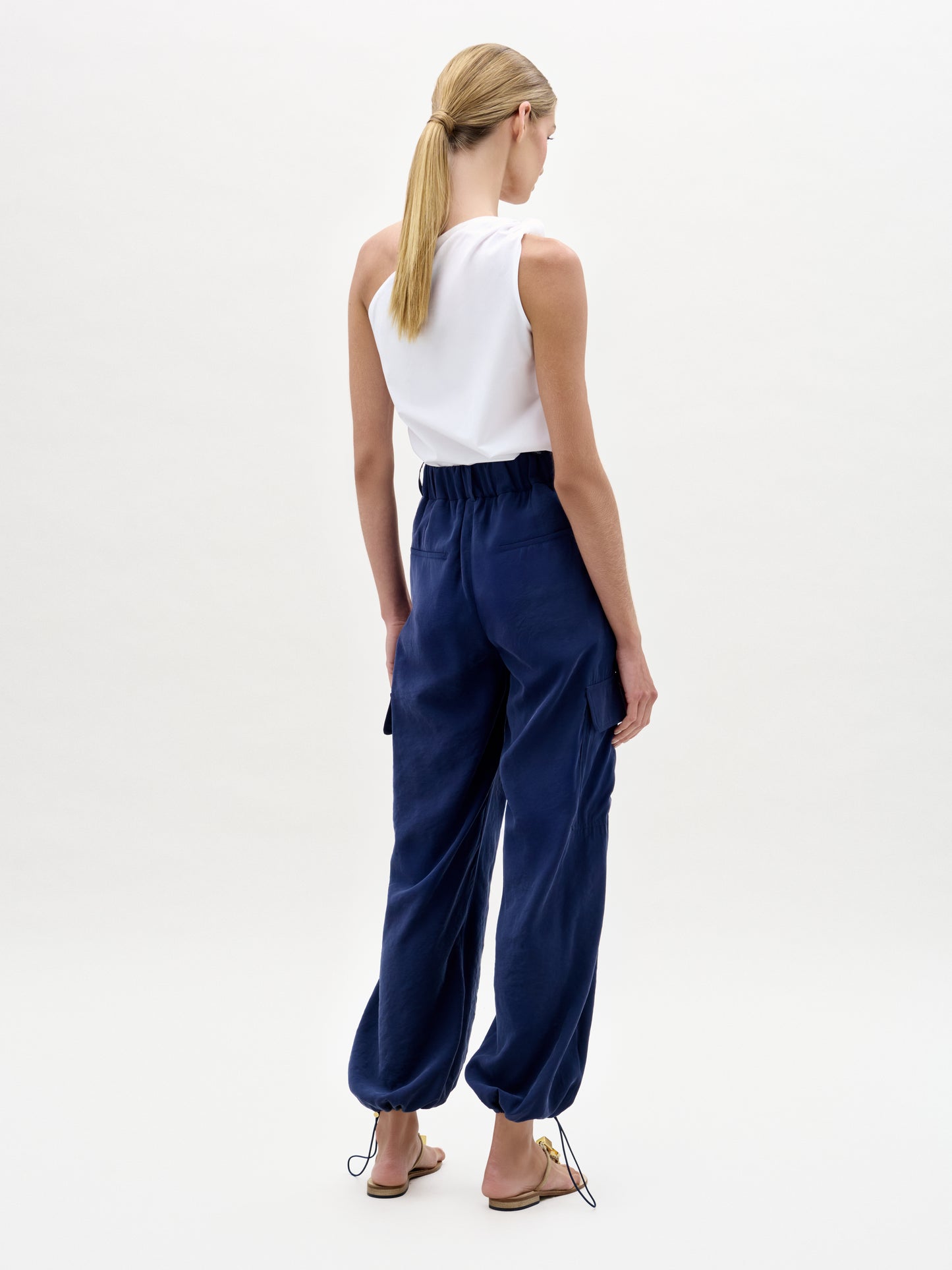 Woman wearing a white sleeveless top and navy blue pants on a white background