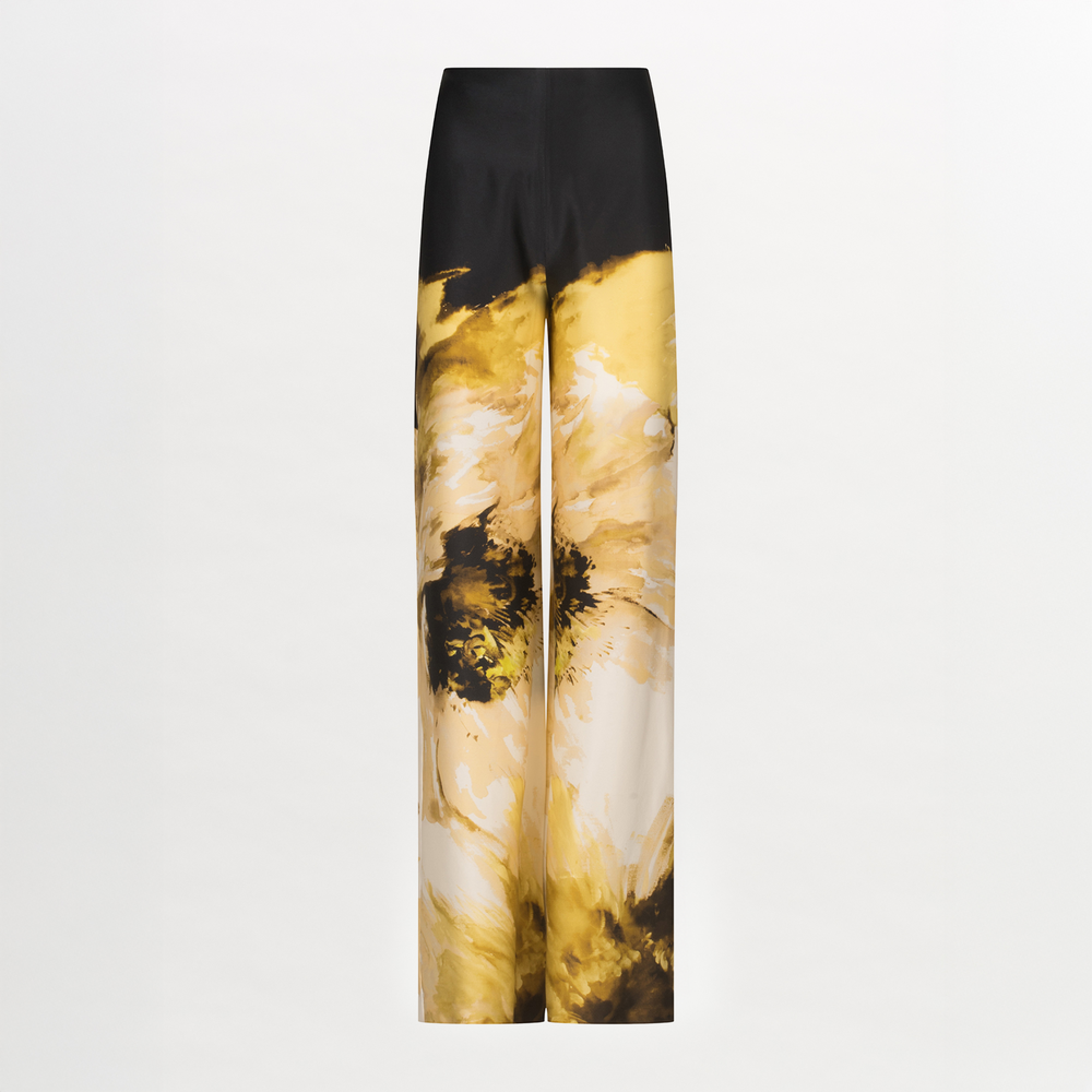 The Andie Pant by Silvia Tcherassi US features a high waist, wide-leg silhouette, and glossy finish. Solid black at the top transitions into bold yellow, beige, and black abstract floral prints along the legs.