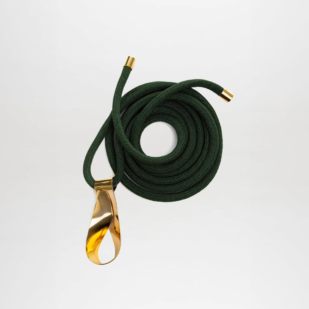 The Daiana Belt by SVT DESIGNS is a coiled dark green Italian cord belt with gold metal end caps and a large smooth gold-plated brass buckle, shown on a plain white background.