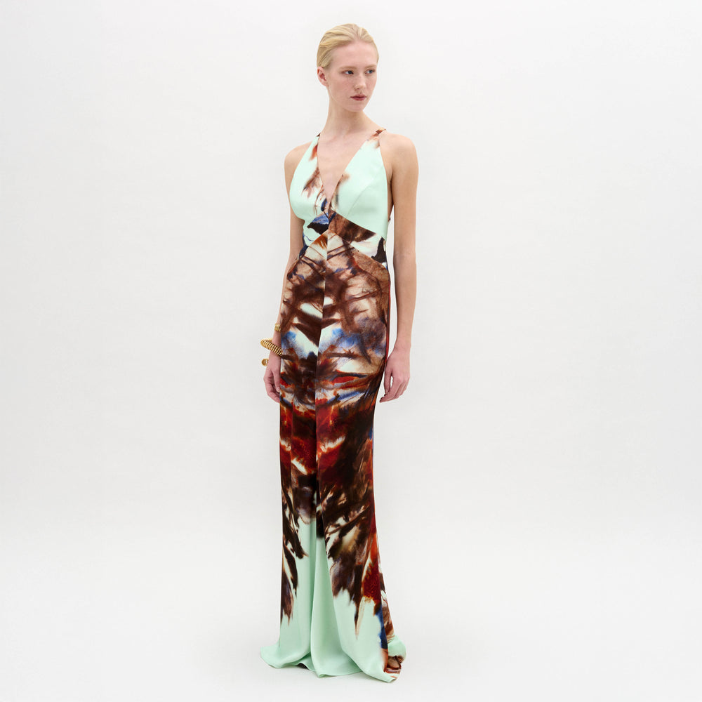 A woman poses in the SVT DESIGNS Daniella Dress, a sleeveless Italian-fabric maxi with a deep V-neckline. The mint green floor-length dress showcases a bold brown and red abstract pattern on the lower half.