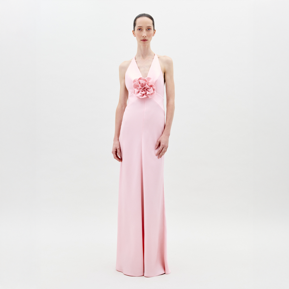 A woman faces forward in the Daniela Dress by SVT DESIGNS—a long pink hammered satin maxi with floral appliqué at the waist. Her hair is pulled back and she stands against a plain white background.