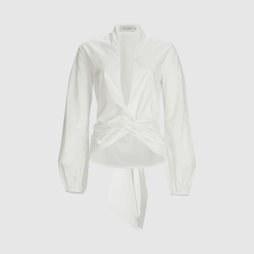 The Dania Blouse by SVT DESIGNS is a white Italian-fabric top with long balloon sleeves, narrow cuffs, a deep V-neck, gathered waist knot, flowing sash, and loose fit for comfort and effortless elegance.