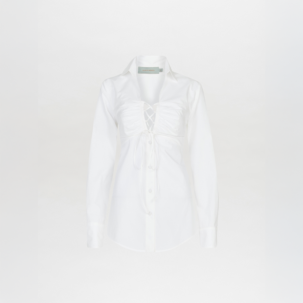 The Dileta Blouse White by Silvia Tcherassi is a crisp cotton, long-sleeve button-up shirt with tailored sleeves, a collared neckline, and front lacing detail with center tie, shown on a plain white background.