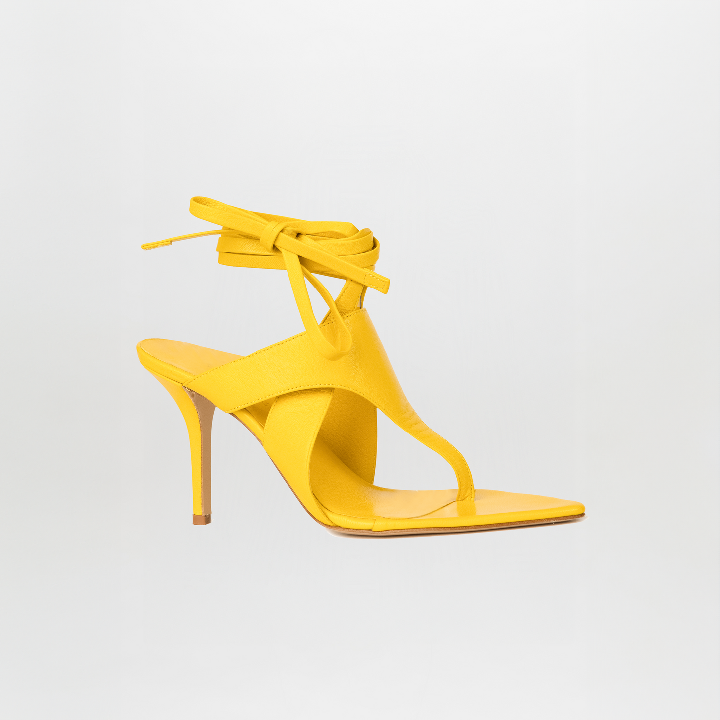 The Domenico Heels Limoncello by SilviaTcherassi are yellow Italian leather heeled sandals with a thong and square toe, ankle wrap laces, and a stiletto heel—the minimal design pops against a plain white background.