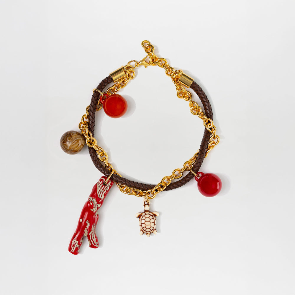 El collar Eira de SVT DESIGNS, con cadena dorada y charms multicolor—varilla roja, tortuga dorada, esfera roja y marrón—resalta sobre fondo blanco.
