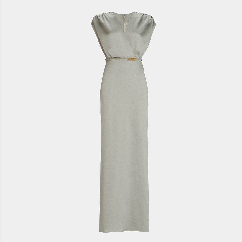 The Freda Dress by SVT DESIGNS is a light gray, floor-length maxi with a V-neckline, sleeveless design, subtle shoulder gathers, a fitted silhouette, and a small metallic accent at the waist.