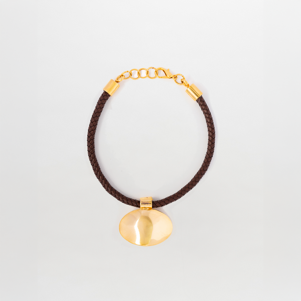 The Gimena Necklace by SVT DESIGNS features a gold pendant with a smooth, rounded shape on a dark brown braided cord with gold accents and an adjustable clasp, shown against a plain white background.