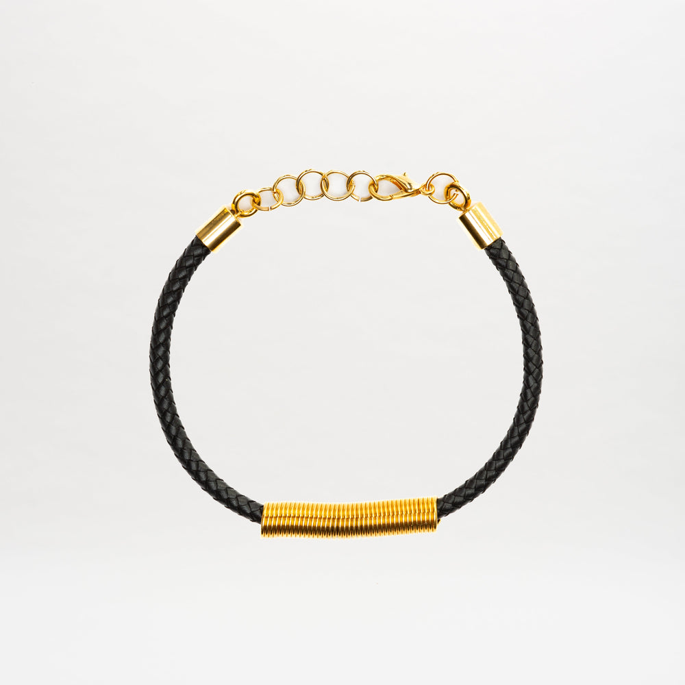 The Hadria Necklace by SVT DESIGNS features a black braided band, gold wire-wrapped accent, an adjustable gold chain clasp, and elegant gold embellishments, displayed on a plain white background.