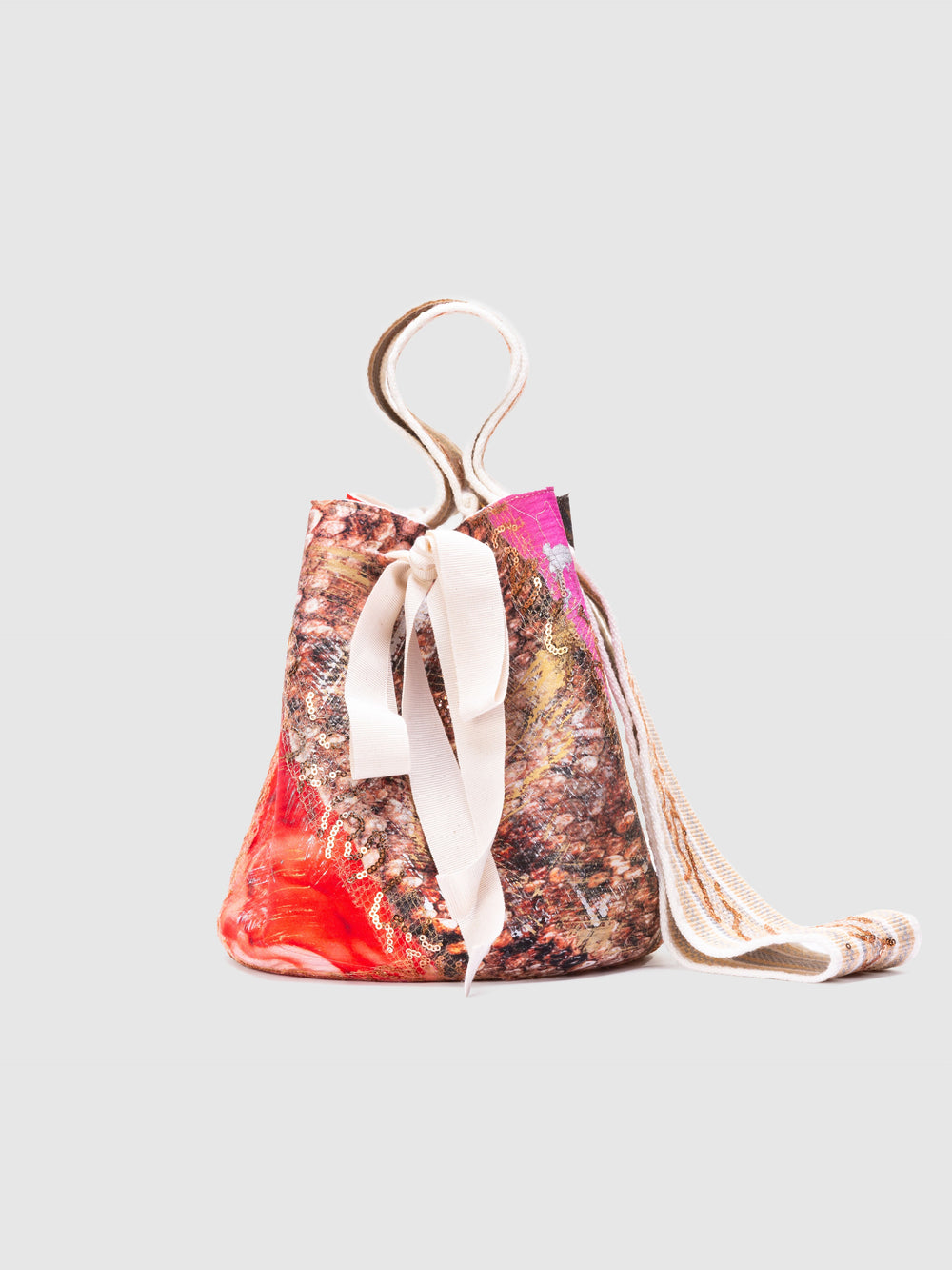 The Mochila Laaput Big by SVT DESIGNS is a handmade bucket bag with a multicolored abstract pattern, a white front ribbon, and a long, thick shoulder strap, shown on a plain light gray background.