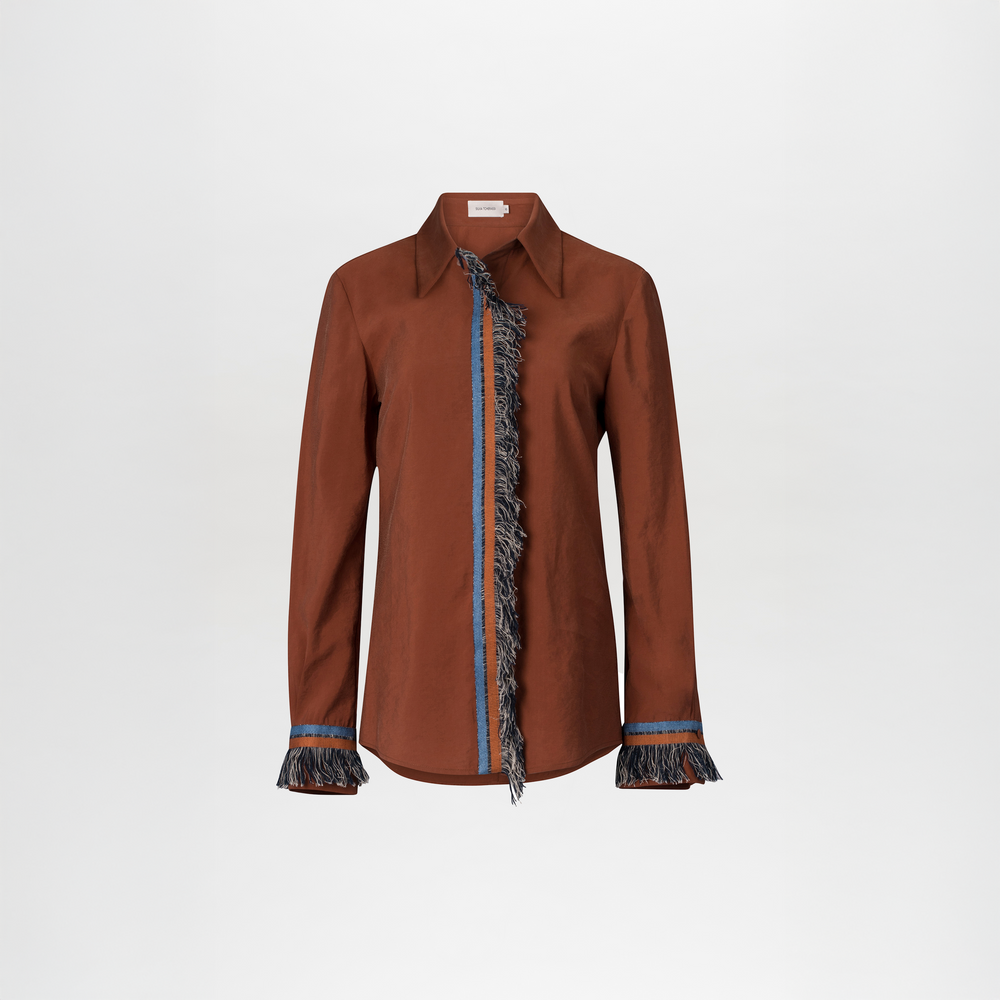 The Liv Blouse by SVT DESIGNS is a brown cotton, long-sleeved top with a shirt collar, accented by blue and black lace fringe trim vertically down the front and cuffs, shown on a plain white background.