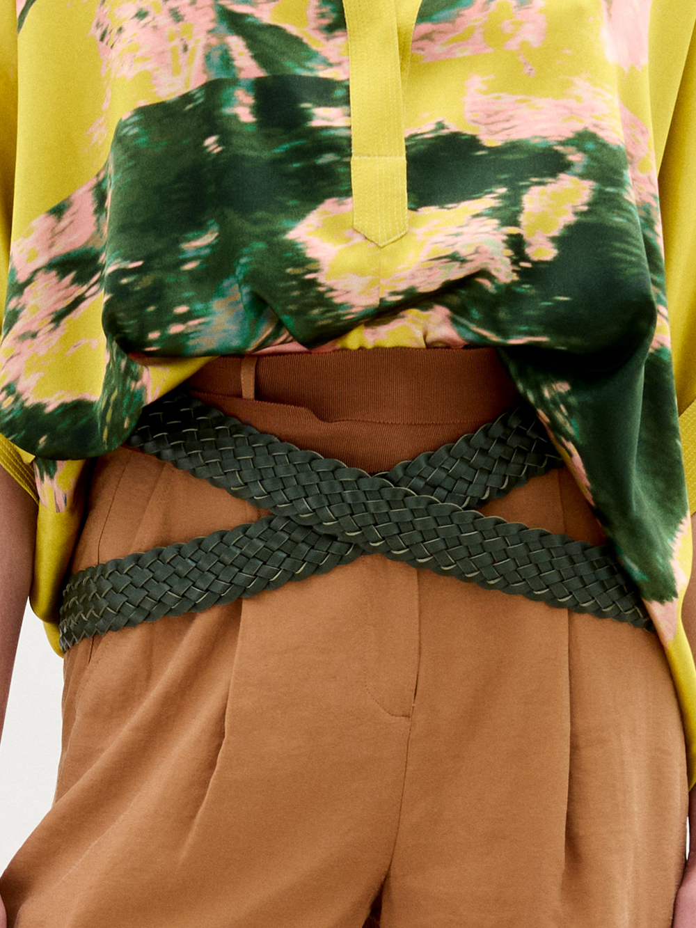 Wearing high-waisted brown pants with the Lauren Belt by SVT DESIGNS crossed at the waist, paired with a yellow and green patterned shirt that's partially tucked in.