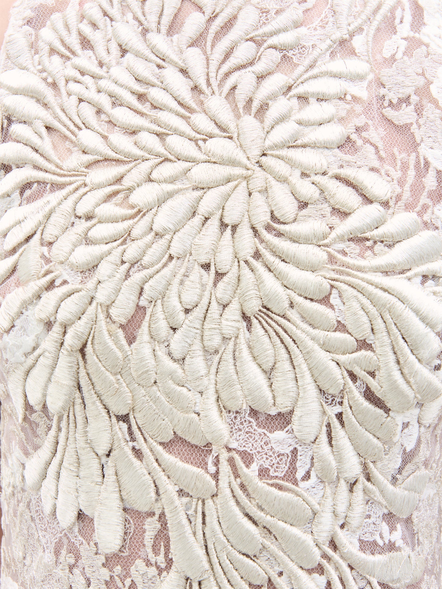 Close-up of intricate floral embroidery on the Levi Dress by SVT DESIGNS. Cream-colored threads create an elaborate raised flower pattern on a sheer, light fabric background, offering a rich and detailed texture.