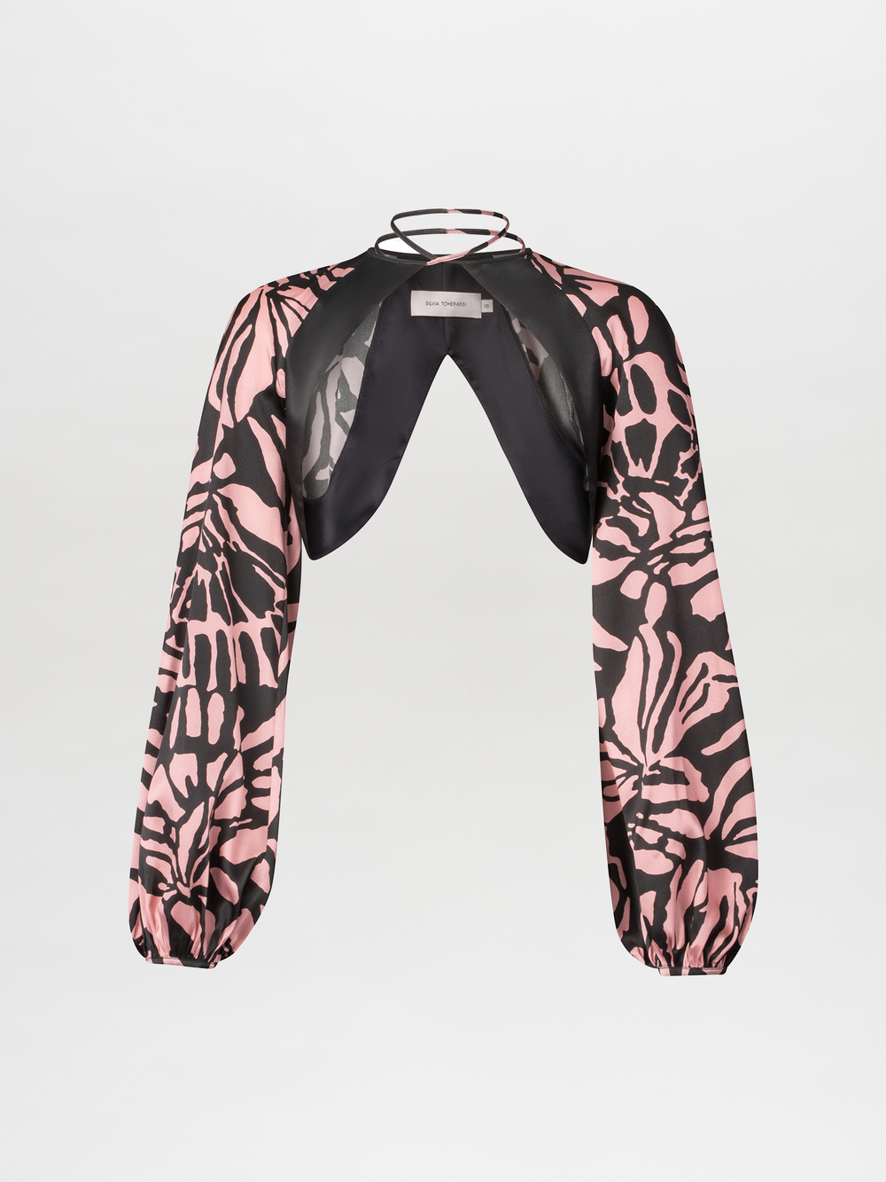 The Moira Cape by SVT DESIGNS is a pink and black abstract print long-sleeve cropped blouse with an open front, gathered cuffs, and a black halter neckline with visible straps, shown on a white background.