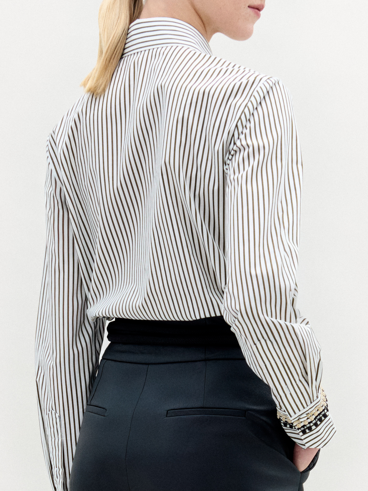 Person stands against a plain background, wearing the Naroa Blouse— a striped 100% cotton button-up— tucked into high-waisted black pants with a gold-buckle belt.