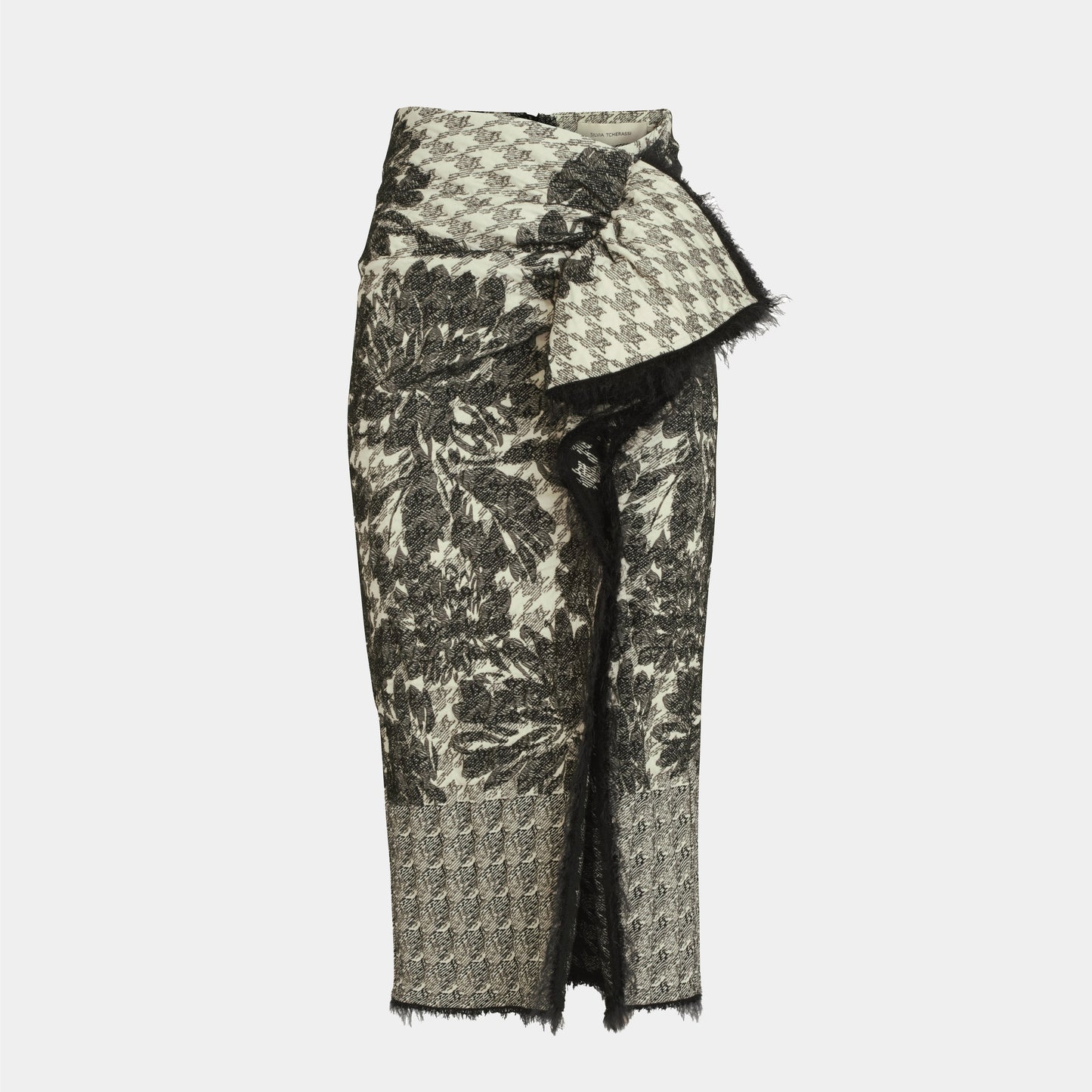 The Nilam Skirt is a high-waisted, knee-length midi with monochrome patchwork, houndstooth and floral patterns, an asymmetrical front fold, draped detail, and raw edges.