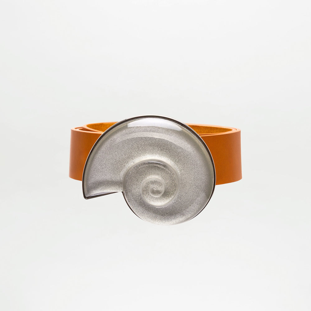 The SVT DESIGNS Nautilus Belt, crafted from 100% brown leather, features a large metallic spiral clasp inspired by a nautilus shell, shown against a plain white background.