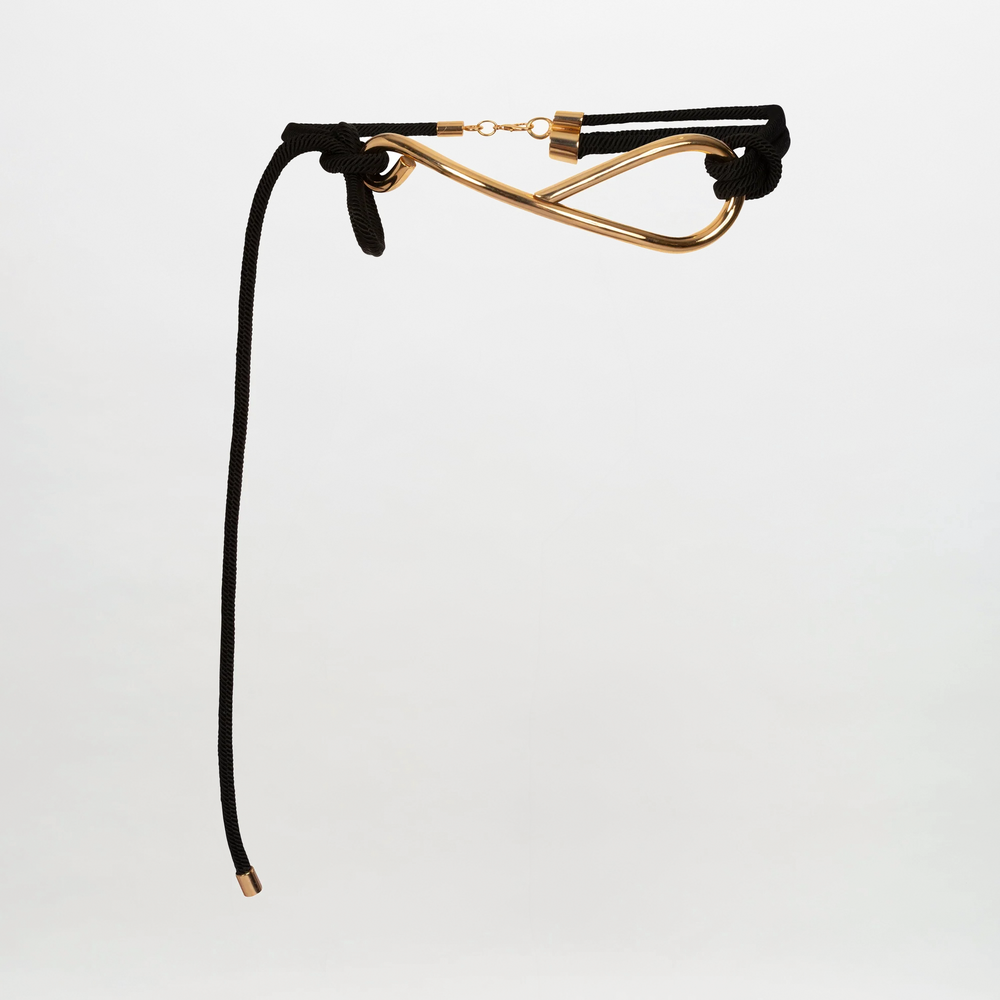 The Pat Belt by SVT DESIGNS features a 3D cord design with gold-tone hardware in a curved, abstract shape. Made in Colombia, it has a top clasp and one loose end, shown against a plain white background.