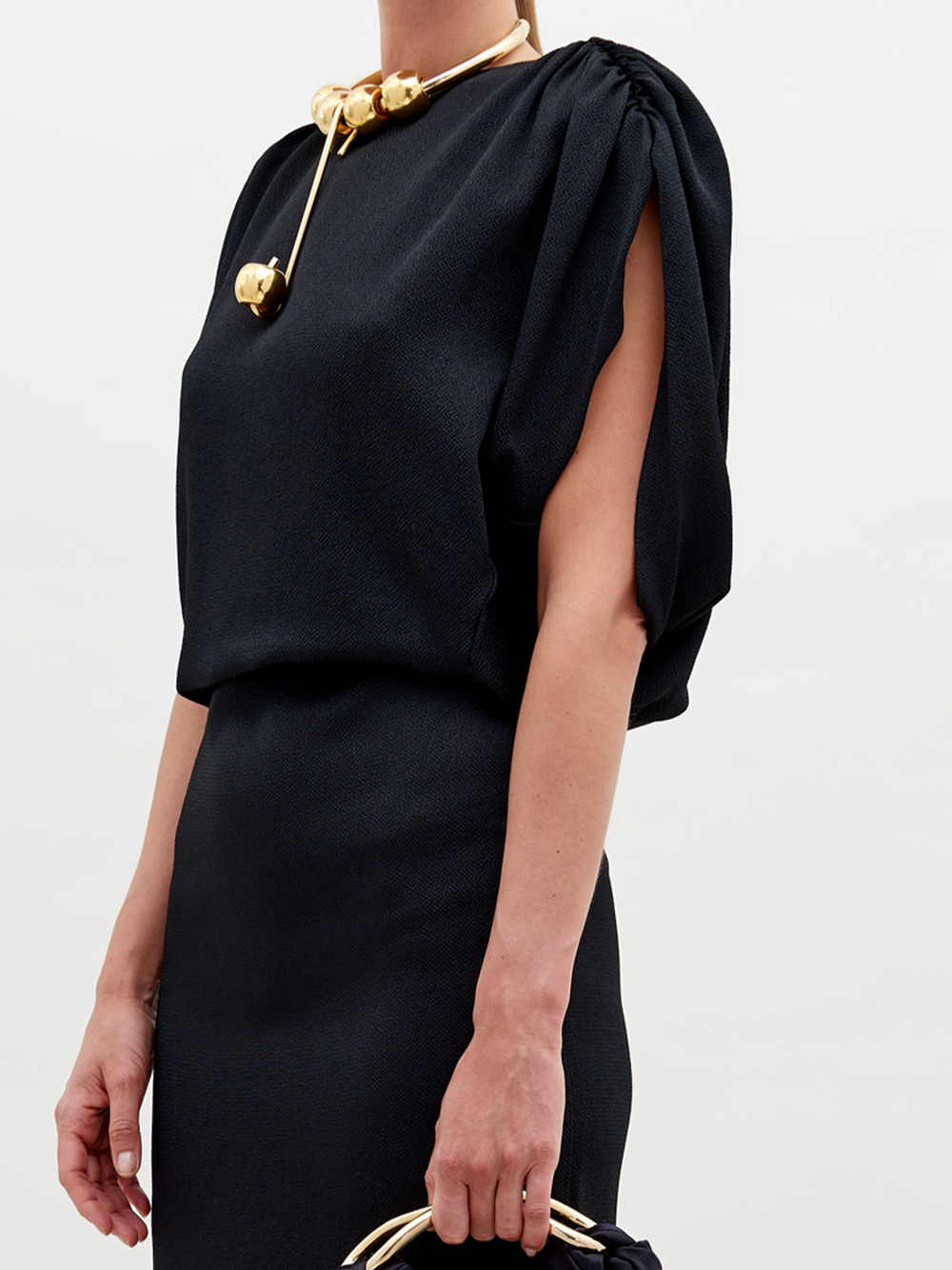 A woman elegantly wears the Reese Dress by SVT DESIGNS, a black midi dress reminiscent of a fitted pencil skirt, exuding sophistication and grace.