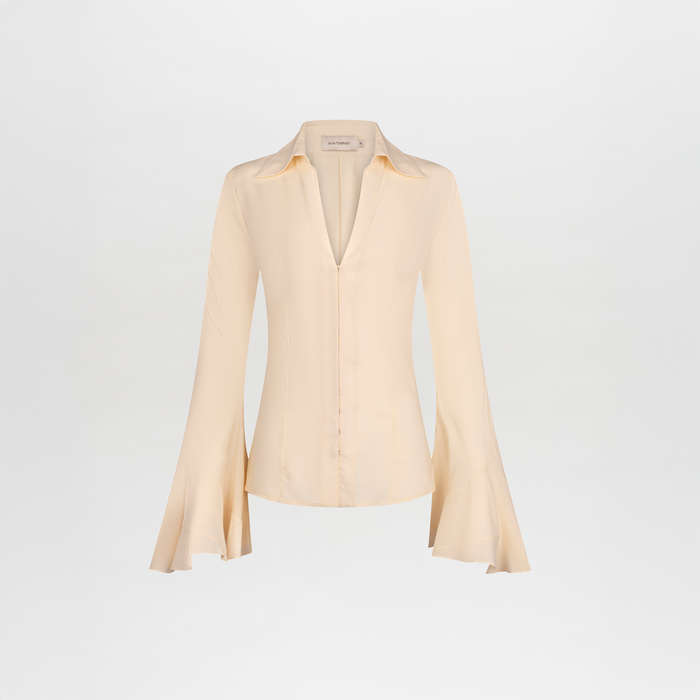 The Reggie Blouse by SVT DESIGNS is a light beige, long-sleeve silk blouse with a collared neckline, bell sleeves, tailored fit, and front buttons, shown on a plain white background.