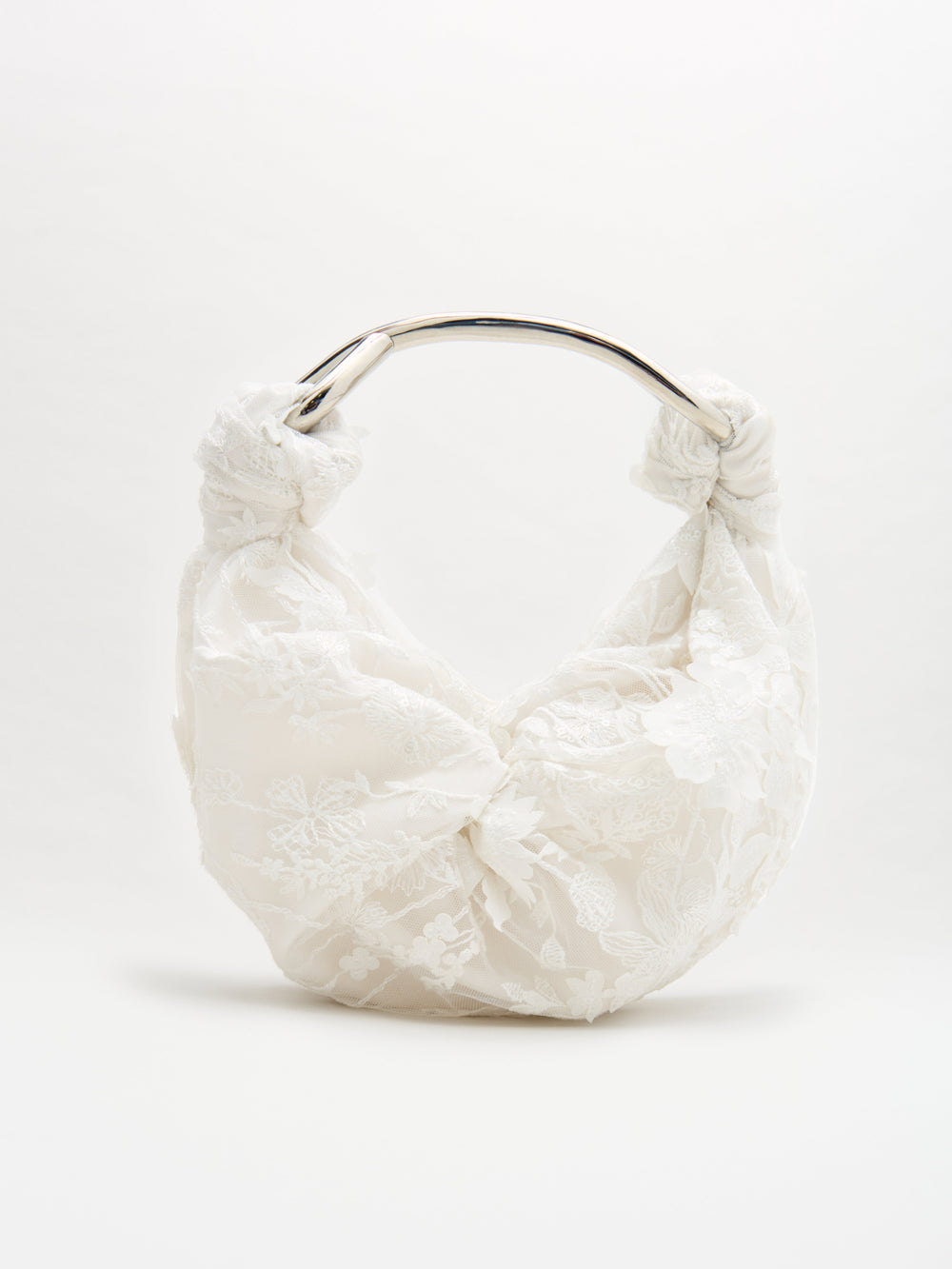 The Sofia Bag Small by SVT DESIGNS is a white handbag with lace floral detailing, made from fine Italian fabric. It features a rounded silver metal handle and a soft, gathered design, shown against a plain white background.