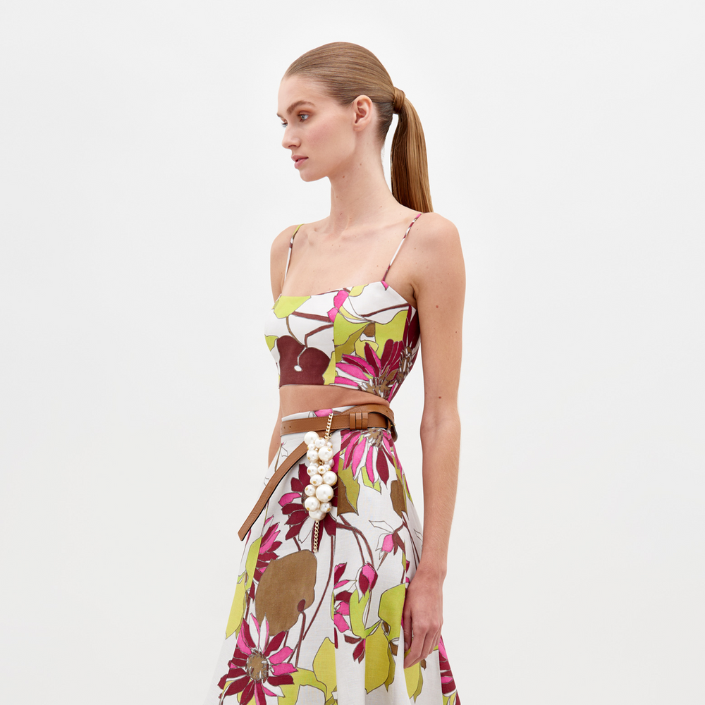 A woman stands against a white background wearing the SVT DESIGNS Trini Top with thin straps and a fitted silhouette. She has a neutral expression and her hair is pulled back in a ponytail.