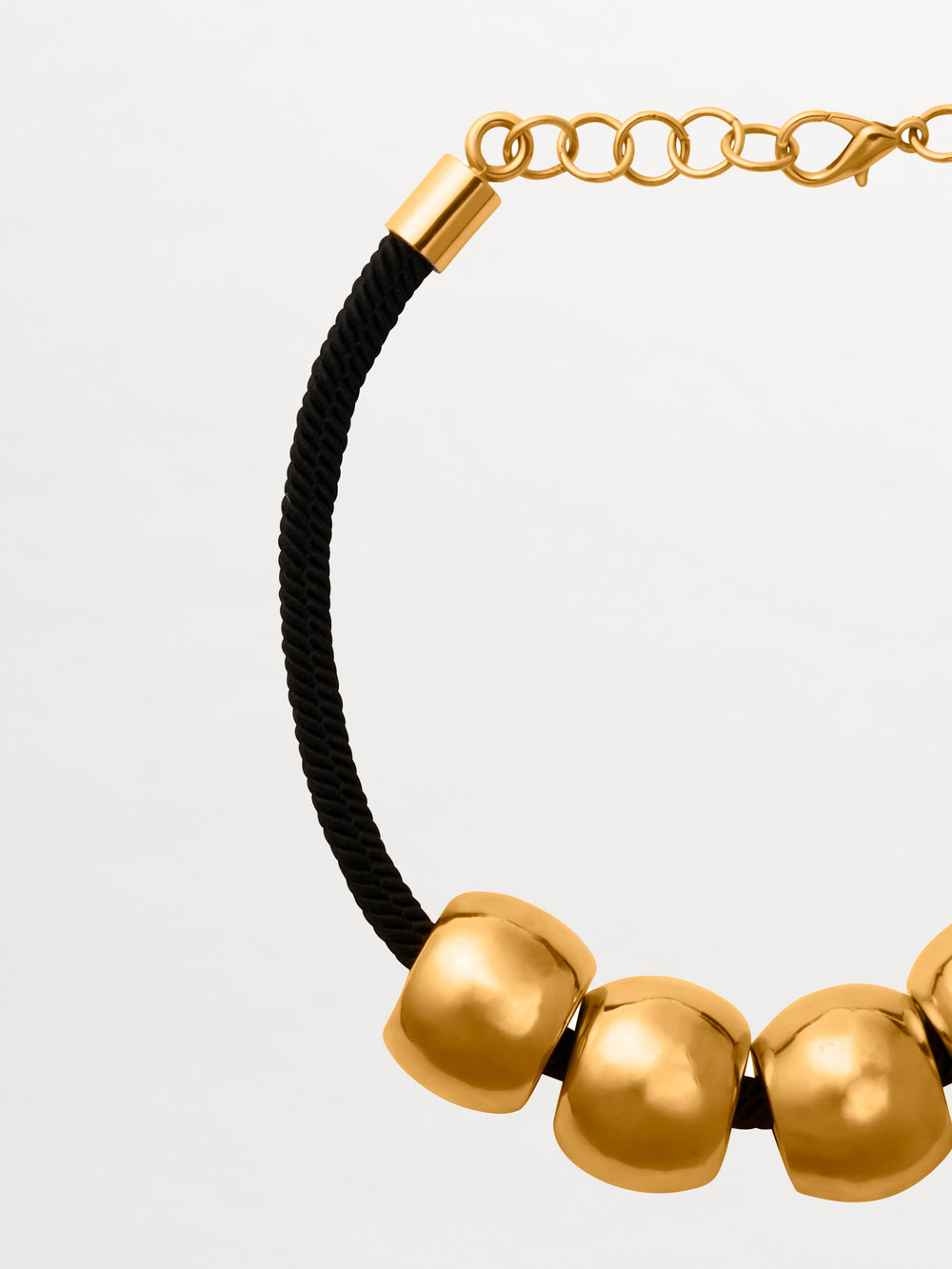 The Tristana Necklace by SVT DESIGNS features a black braided cord, four large gold-toned rounded beads with elegant gold accents, and a gold clasp with an adjustable chain. Displayed against a simple light background.