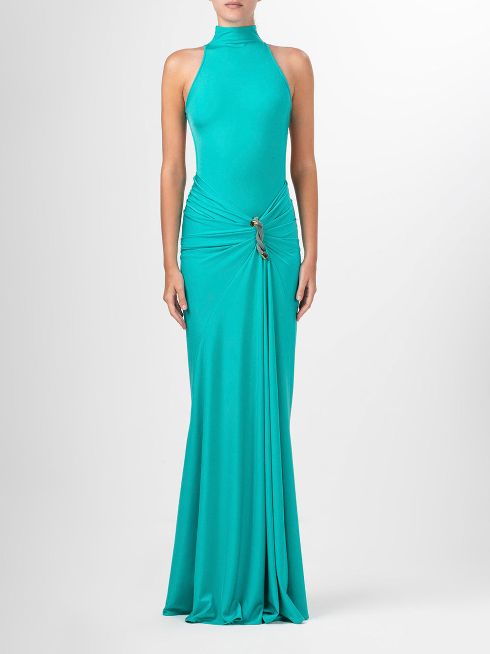 A person wears the Claudia Skirt by Silvia Tcherassi US, featuring a sleeveless, turquoise halter-neck design with a draped silhouette. The dress has a gathered waist with metallic embellishments and elegantly flows into a floor-length maxi skirt against a plain white background.