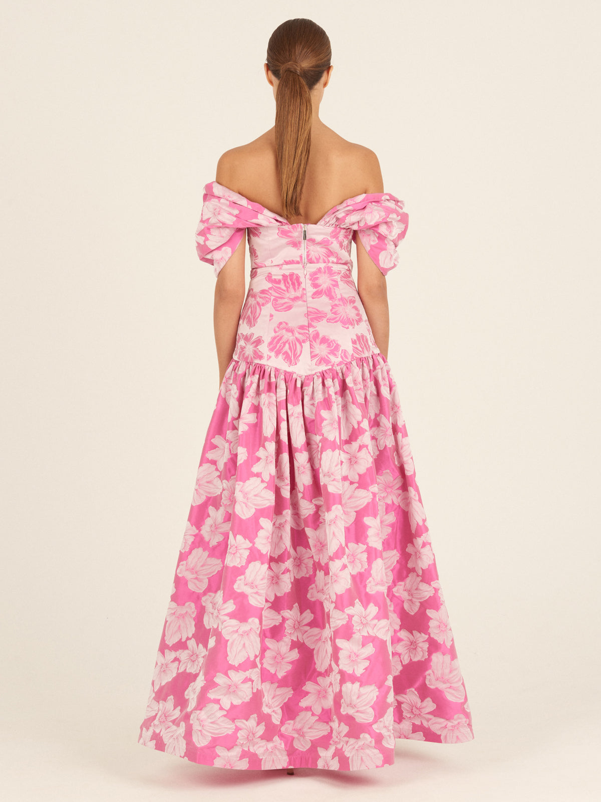 A woman with straight brown hair in a low ponytail is seen from behind wearing the Silvia Tcherassi Danu Skirt in Magenta Floral, featuring puffed sleeves and a full, floor-length silhouette.