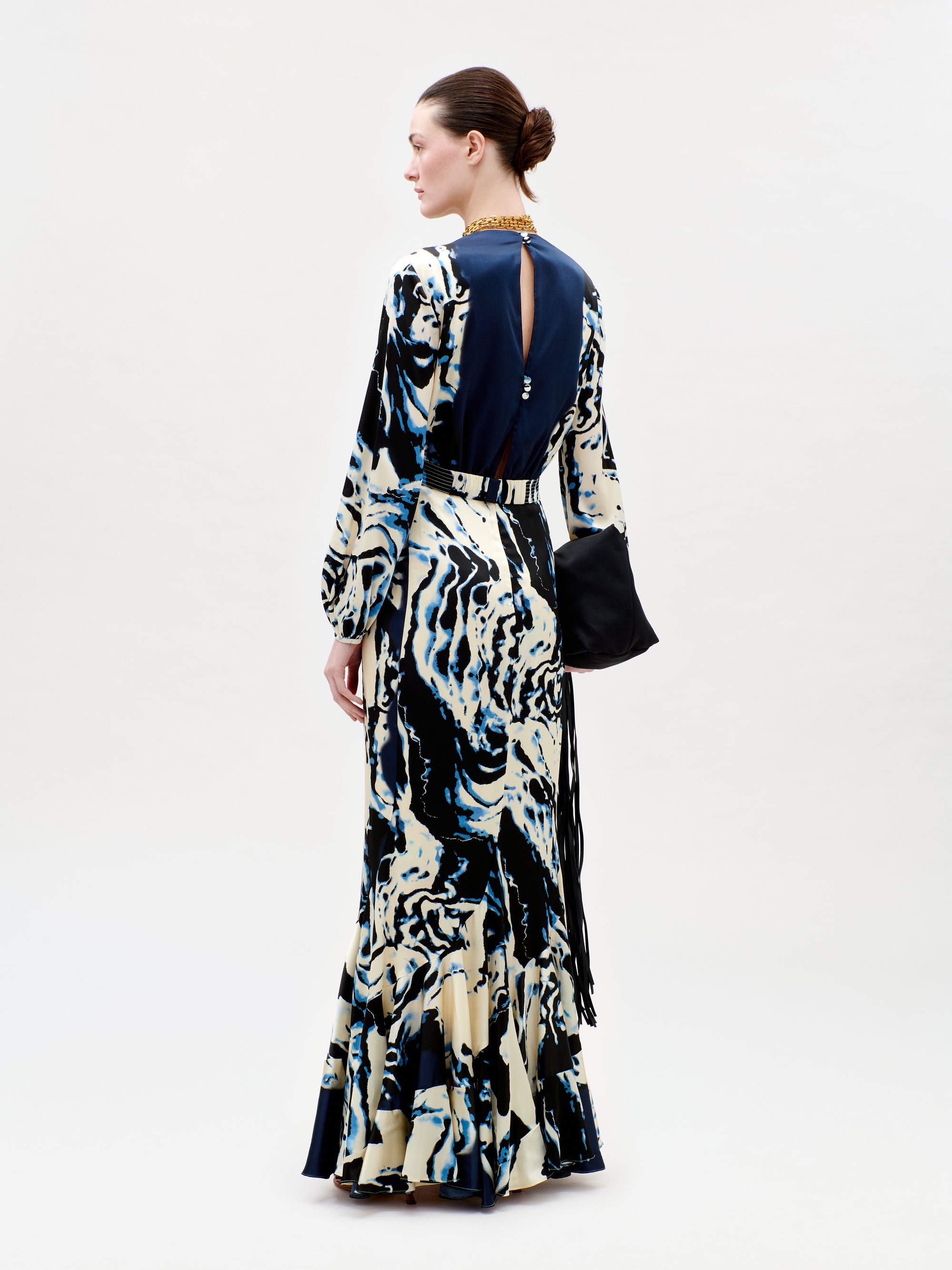 Woman wearing a long, patterned dress with a black handbag on a white background