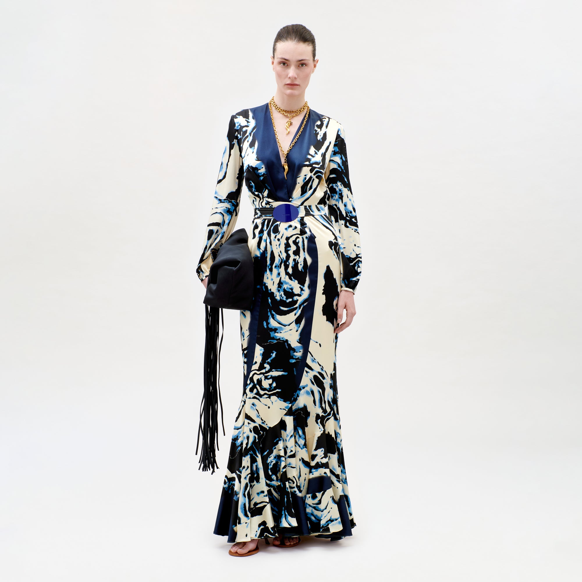 Model wearing a long, patterned dress with a black handbag on a white background