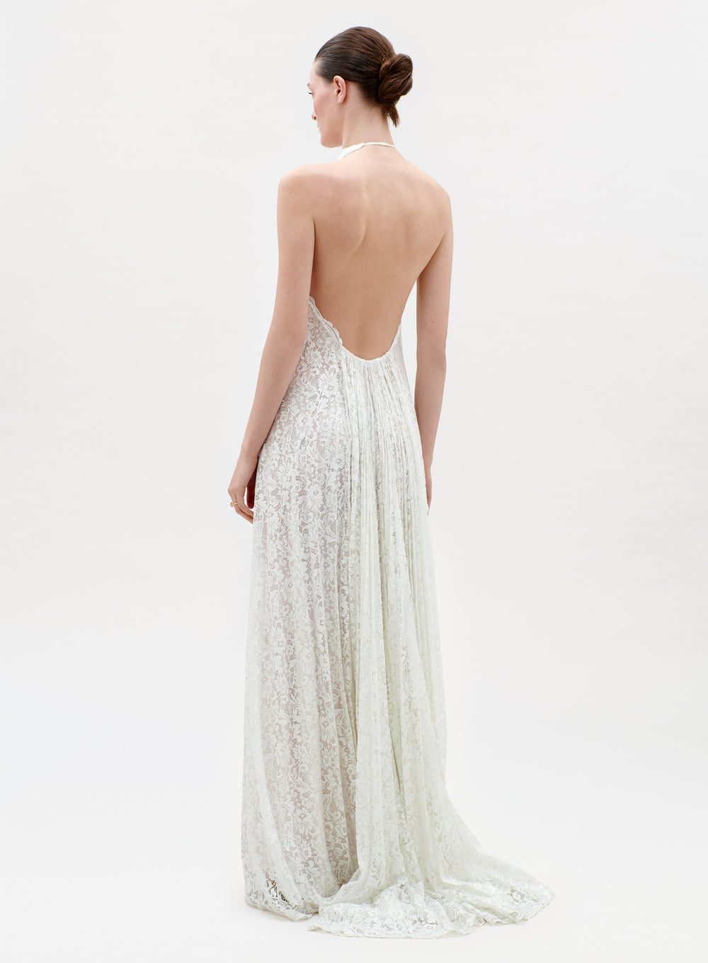 Woman wearing a long, elegant white dress with an open back on a light background