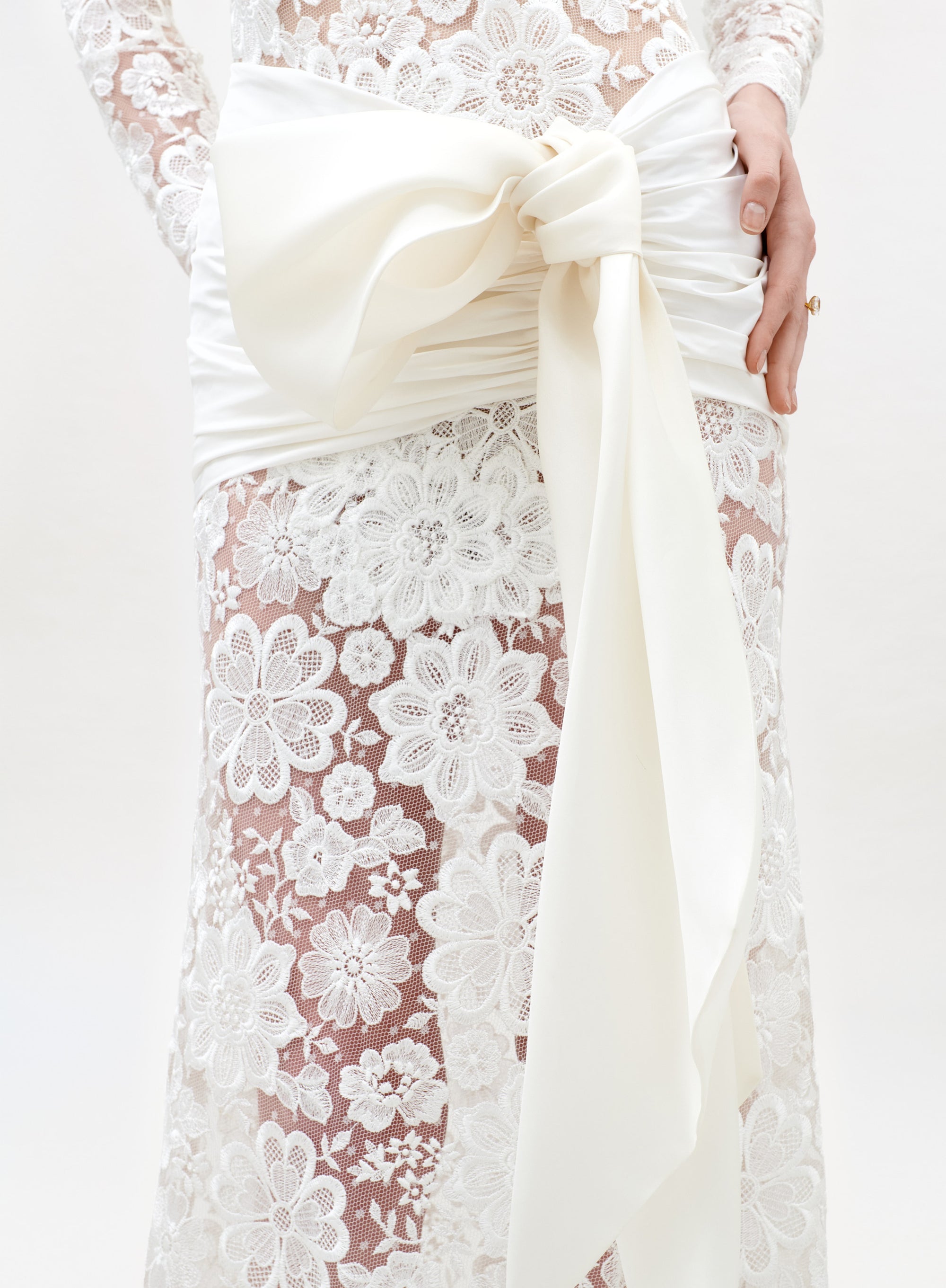 Close-up of a white lace dress with a large bow on a white background
