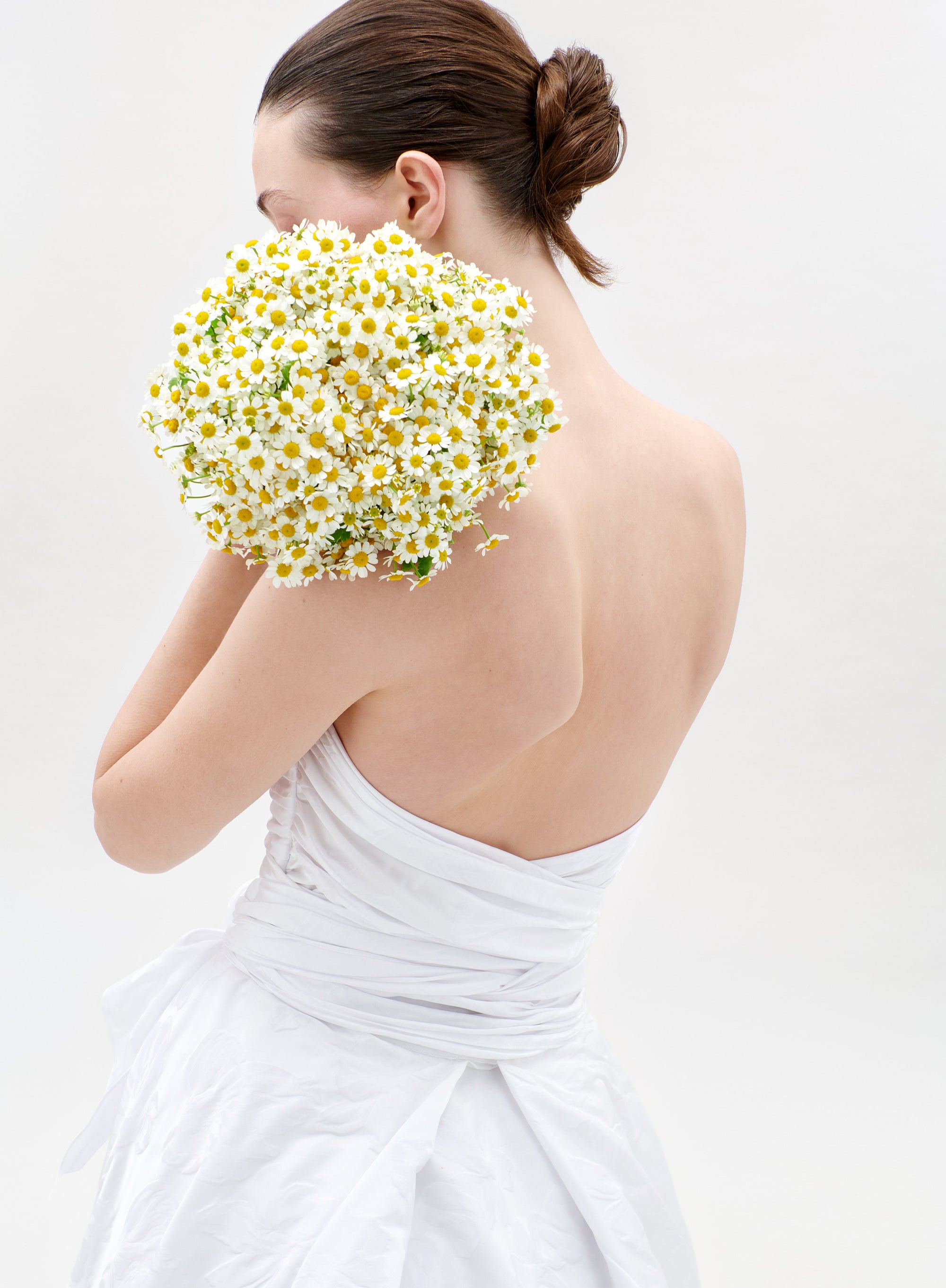 Woman in a white dress holding a bouquet of daisies against a light background