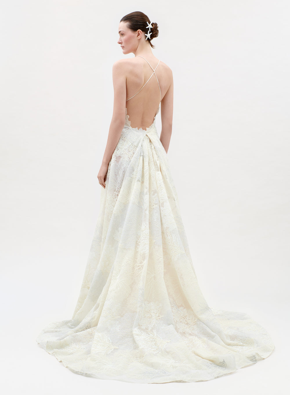 Woman wearing a white wedding dress with a flowing train on a plain background