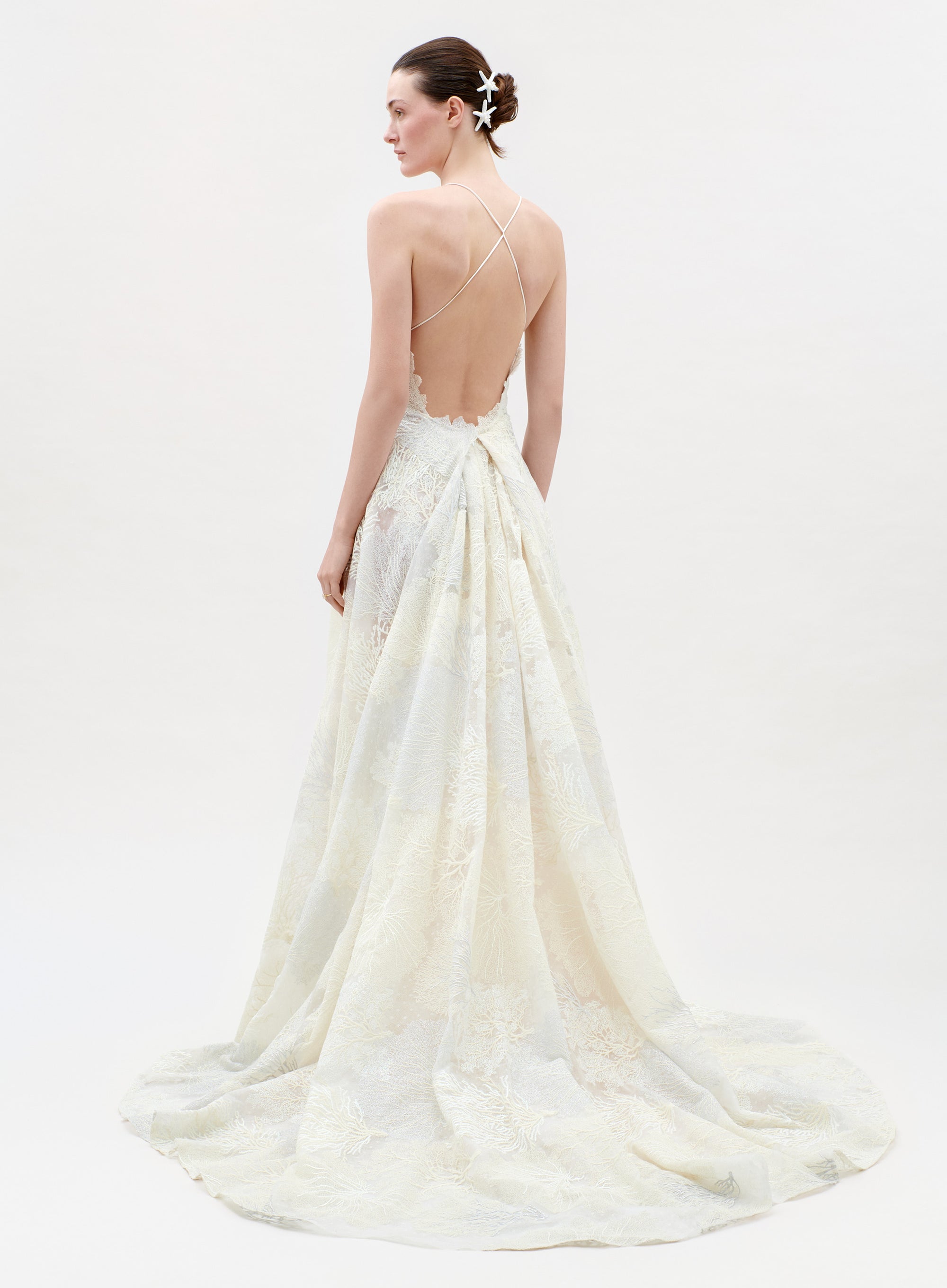 Woman wearing a white wedding dress with a flowing train on a plain background