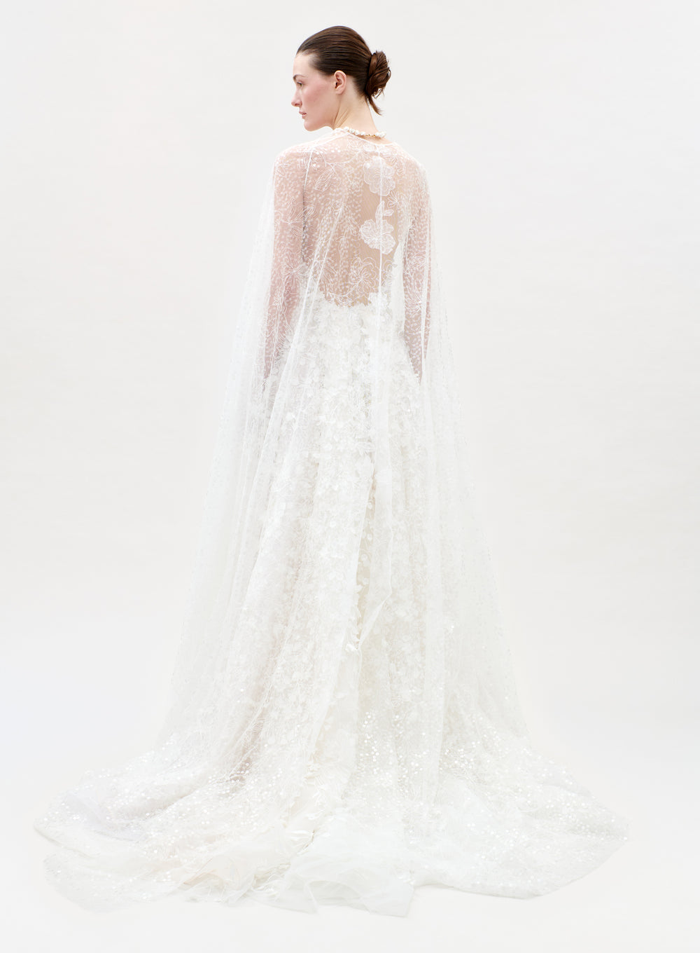 Woman wearing a white lace wedding dress with a sheer overlay on a white background