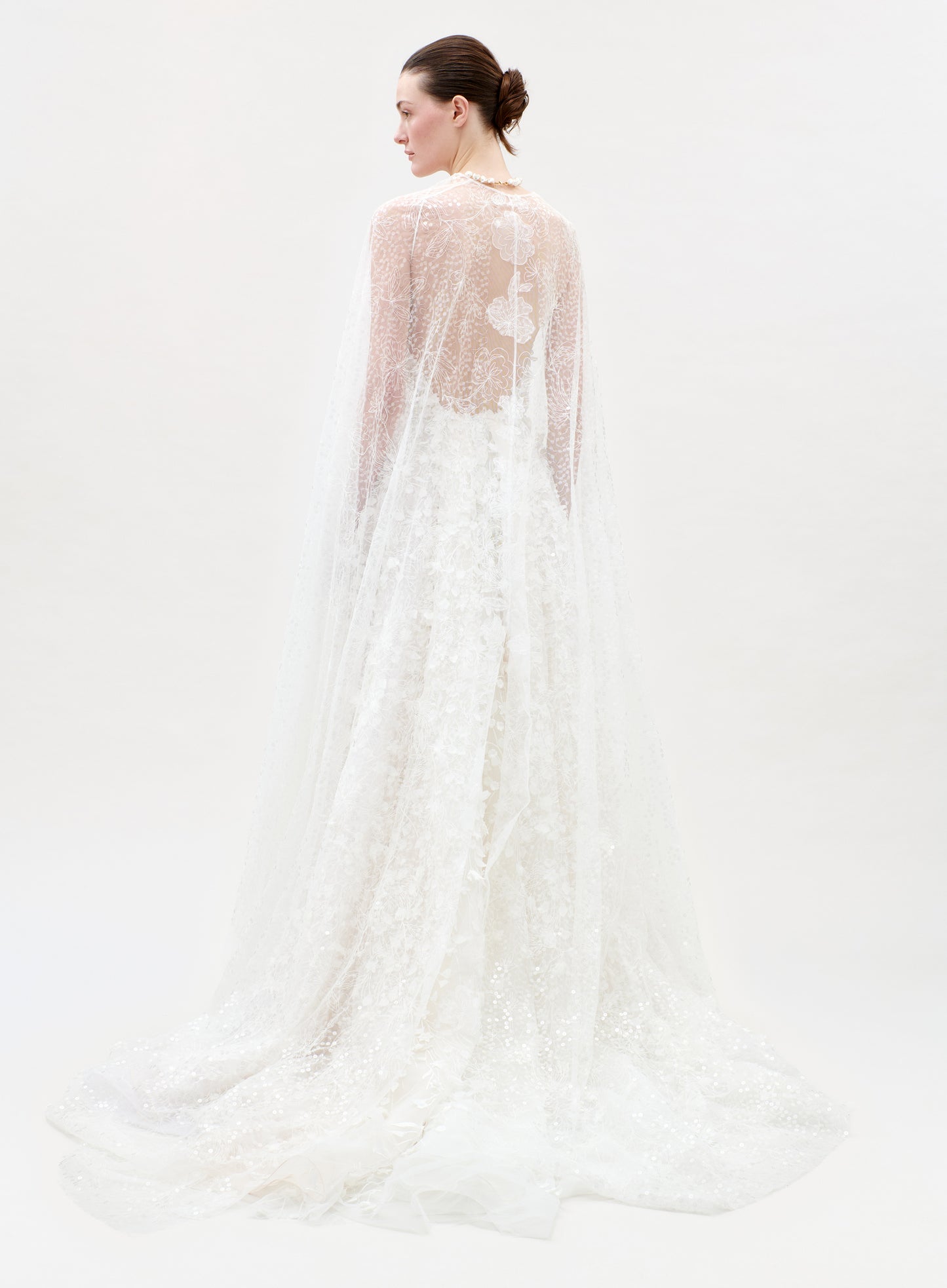 Woman wearing a white lace wedding dress with a sheer overlay on a white background