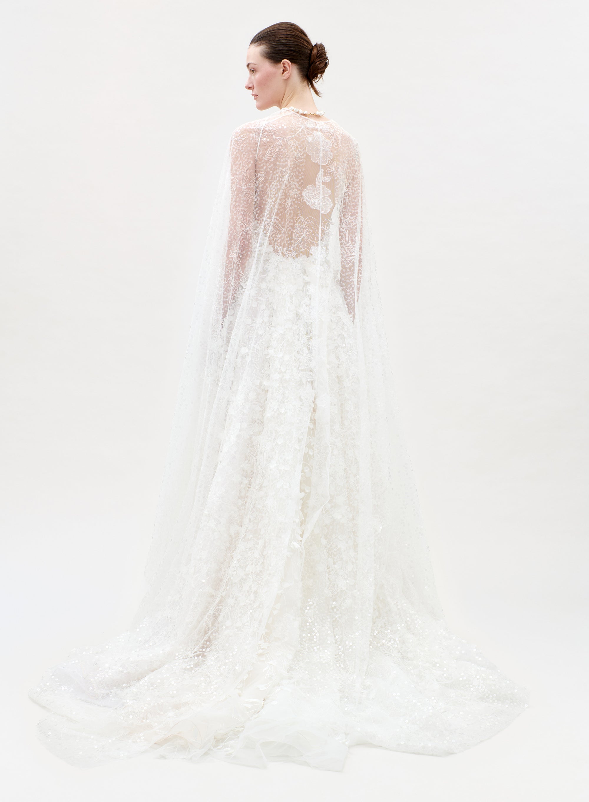 Woman wearing a white lace wedding dress with a sheer overlay on a white background