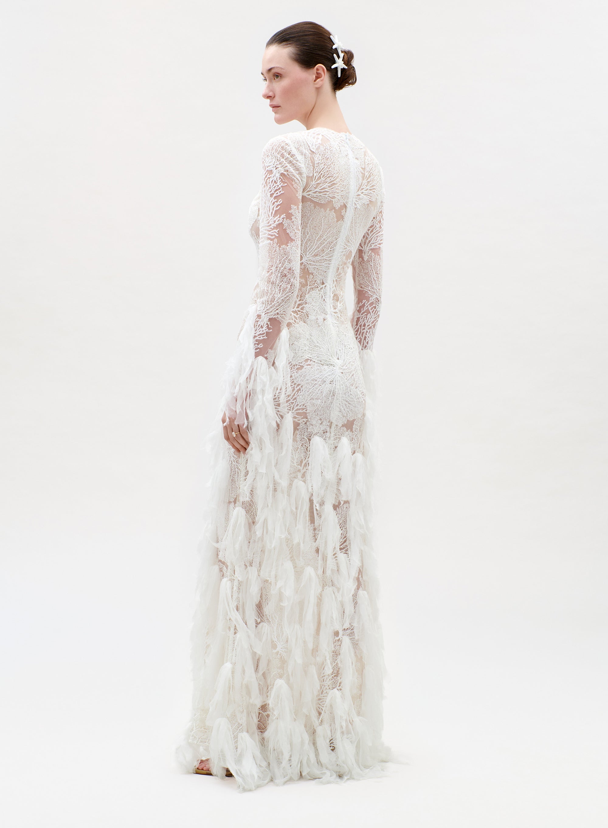 Woman wearing a long, white lace dress on a plain background