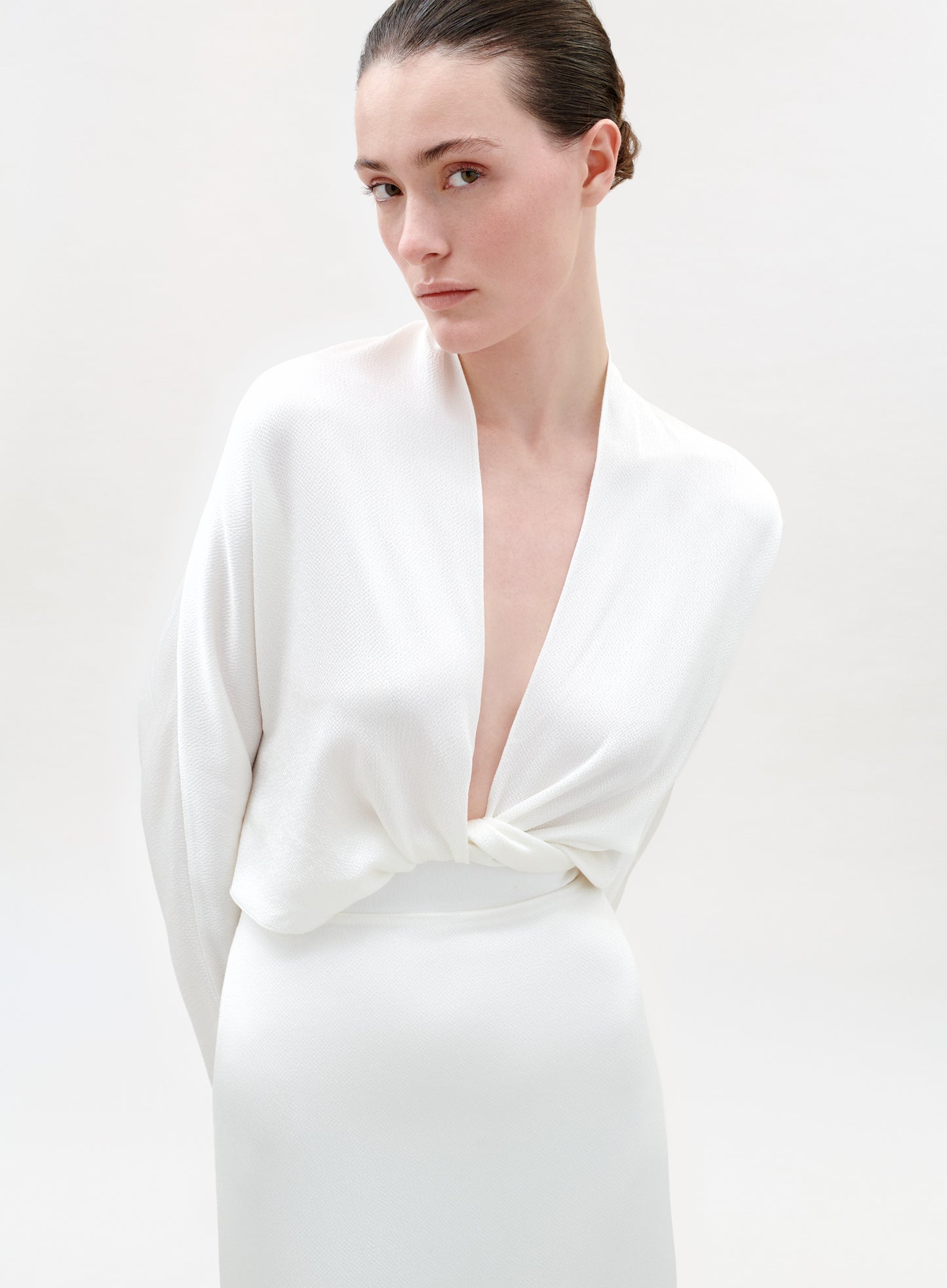 Woman wearing a white dress with a deep neckline on a plain background