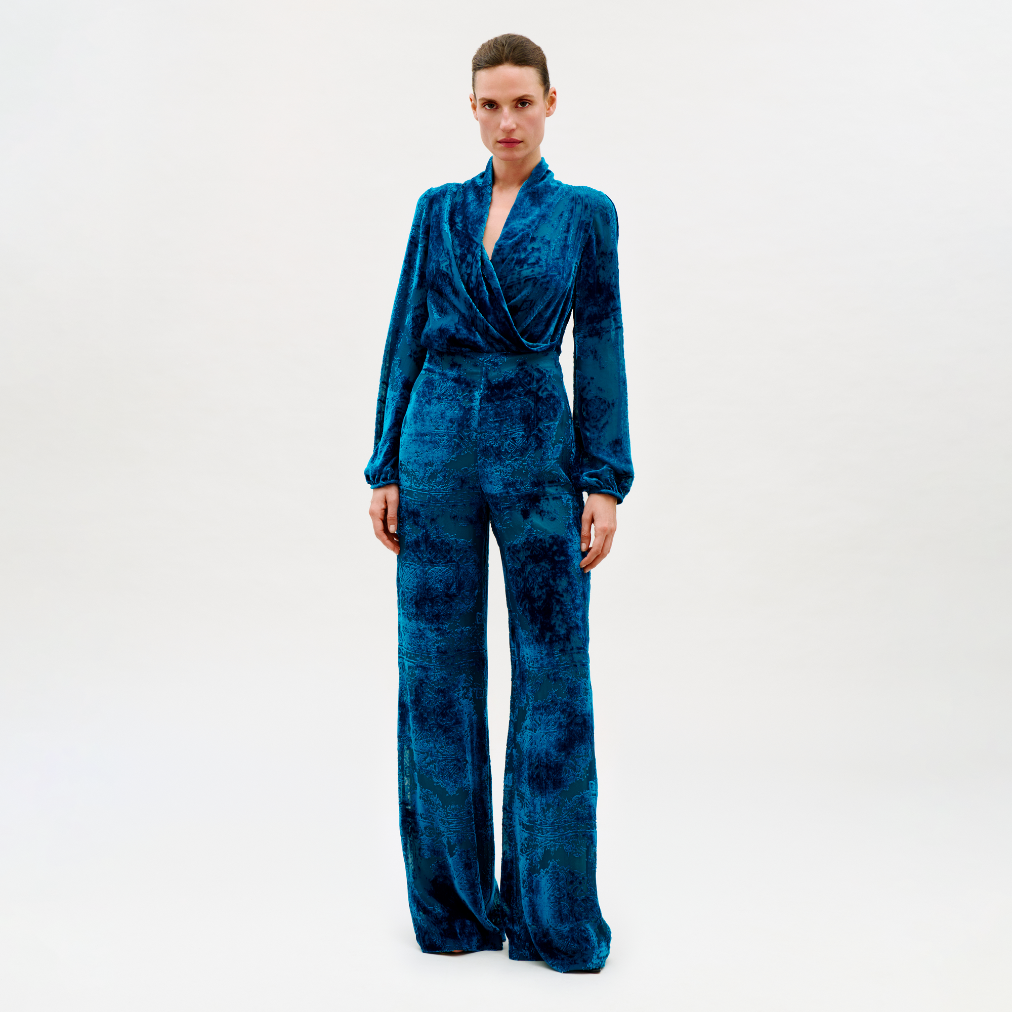 Woman wearing a blue velvet jumpsuit on a white background