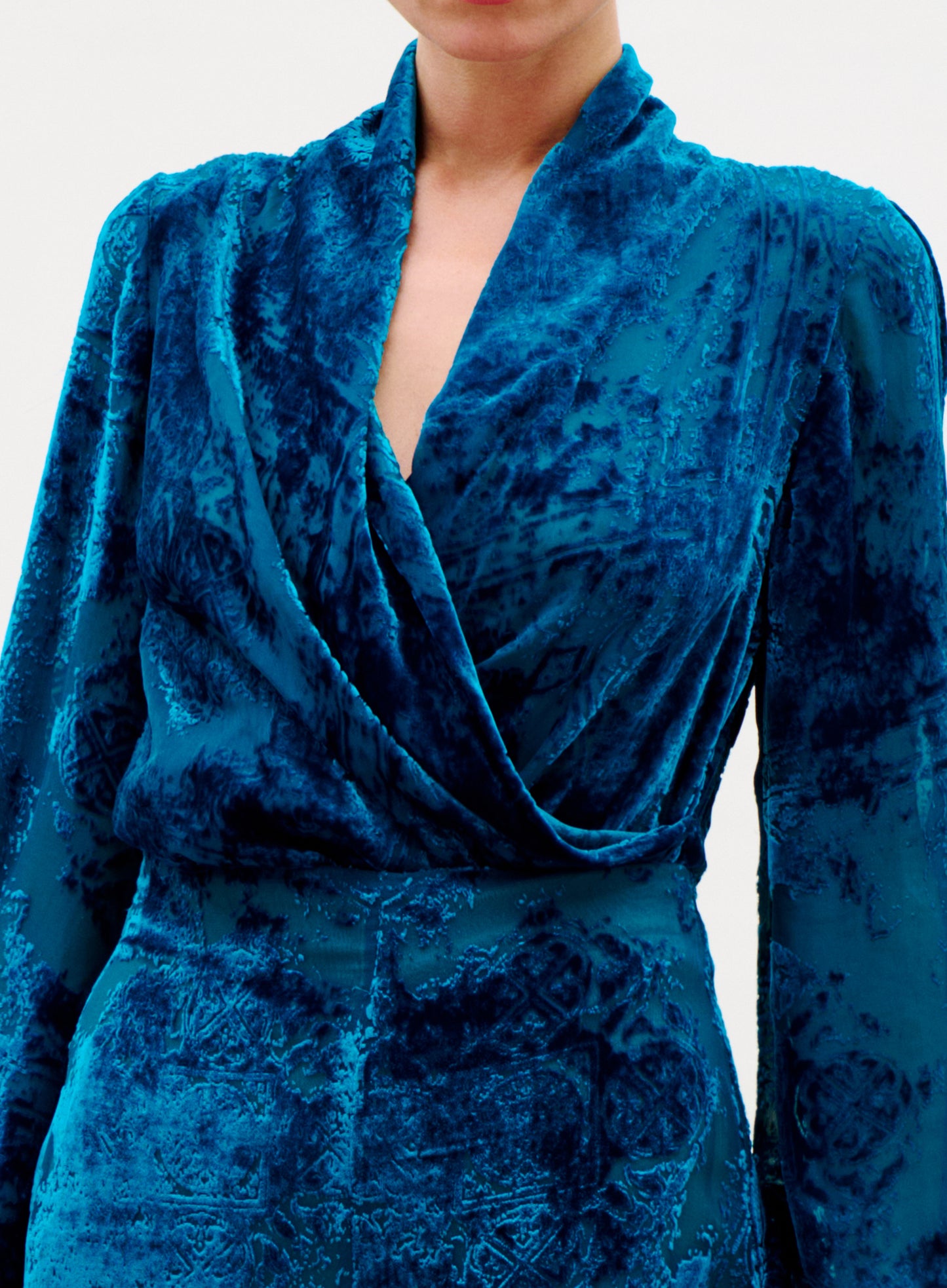 Blue velvet dress with a draped neckline on a plain background