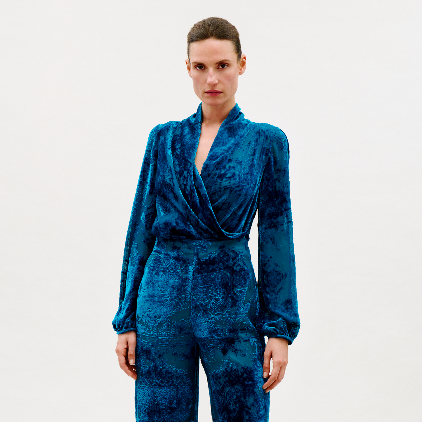 Woman wearing a blue velvet jumpsuit on a white background