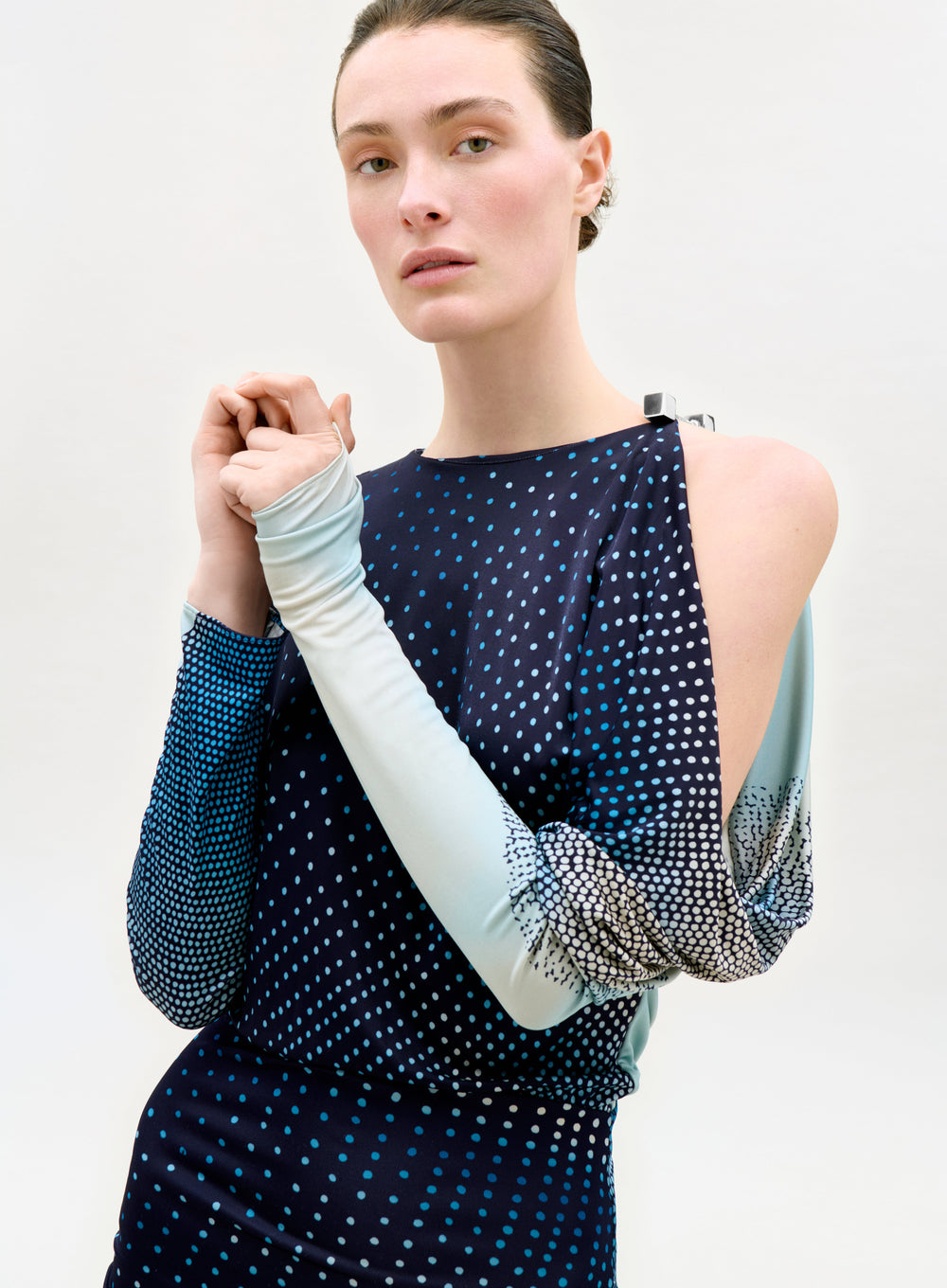 Woman wearing a dark blue dress with cut-out shoulders and light blue gloves against a white background