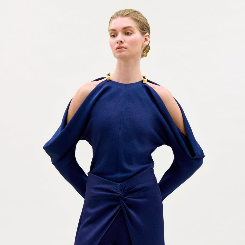 Woman wearing a blue dress with cut-out shoulders on a light gray background