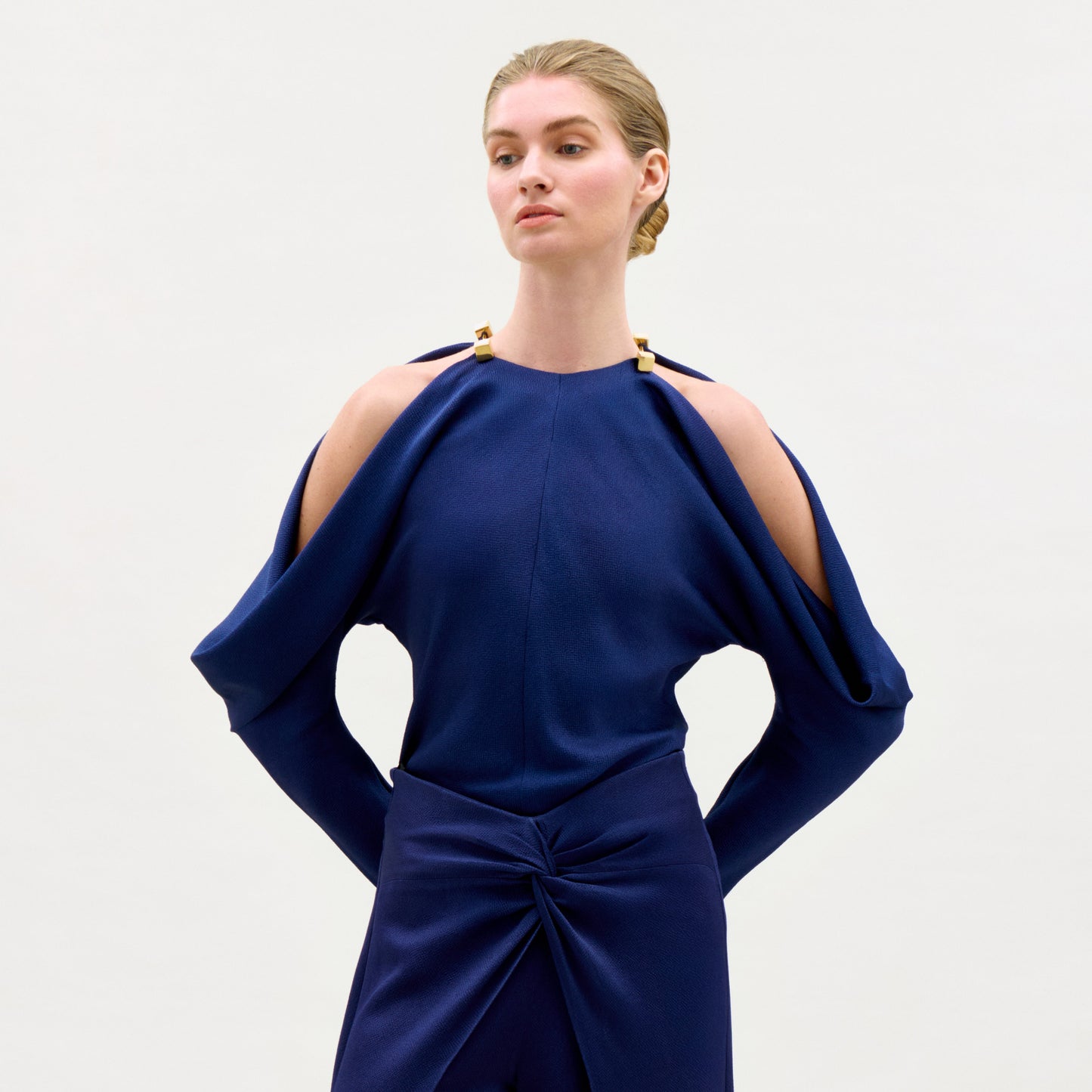 Woman wearing a blue dress with cut-out shoulders on a light gray background